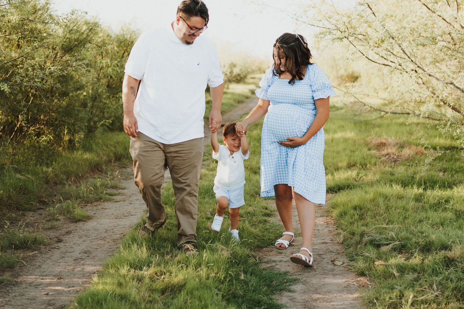 Family walking together on grassy path during golden hour photoshoot.