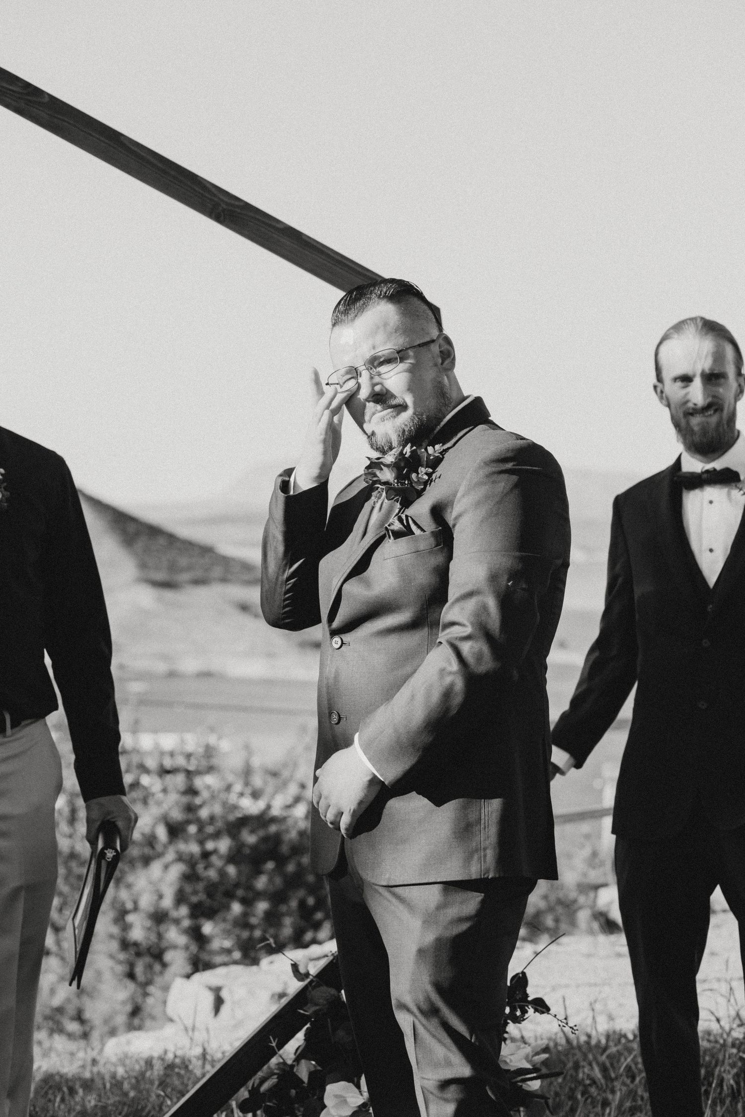 A row of men in suits and bowties showing emotional reactions at an outdoor event.
