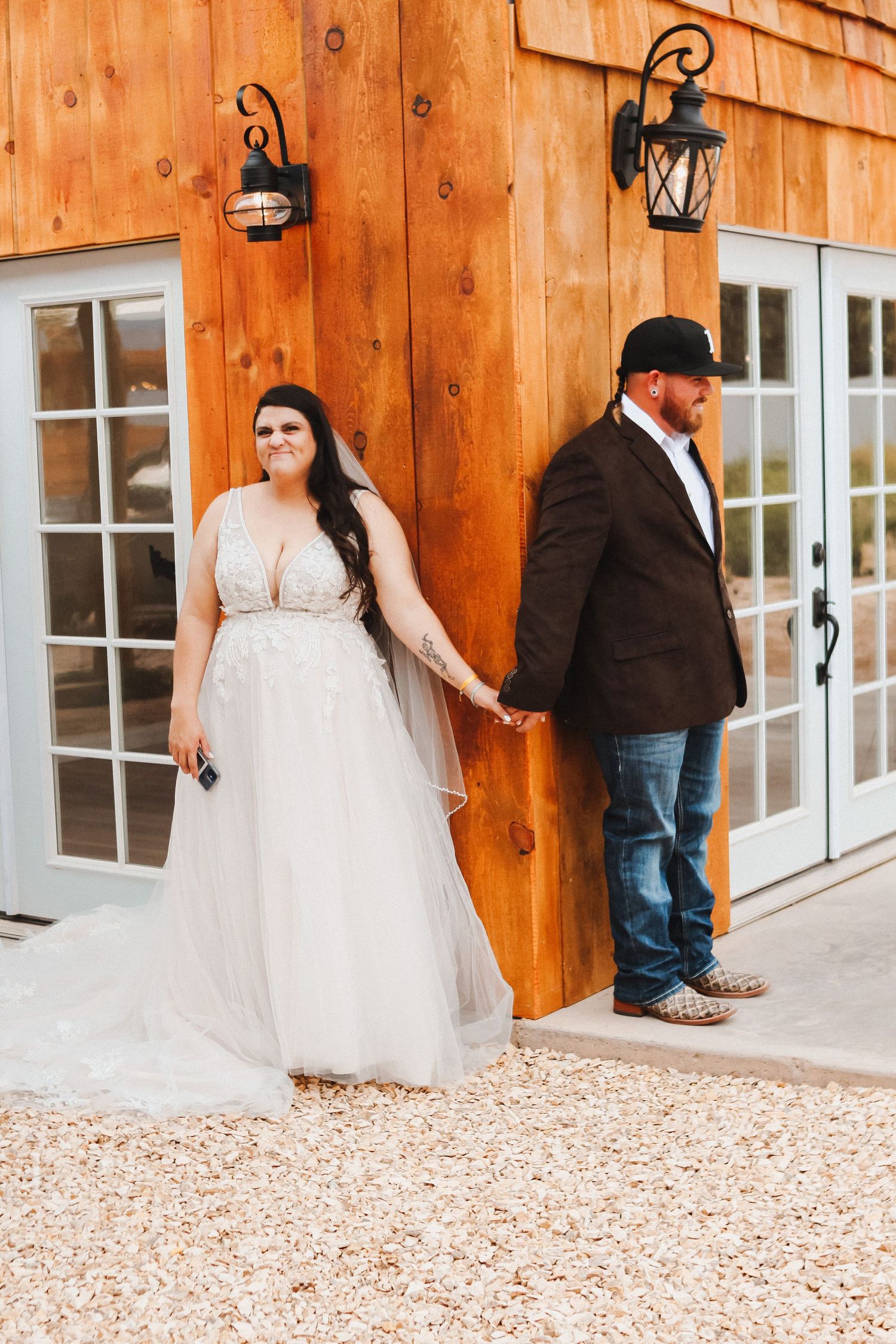 First look wedding photo against rustic wooden wall with lantern sconces.