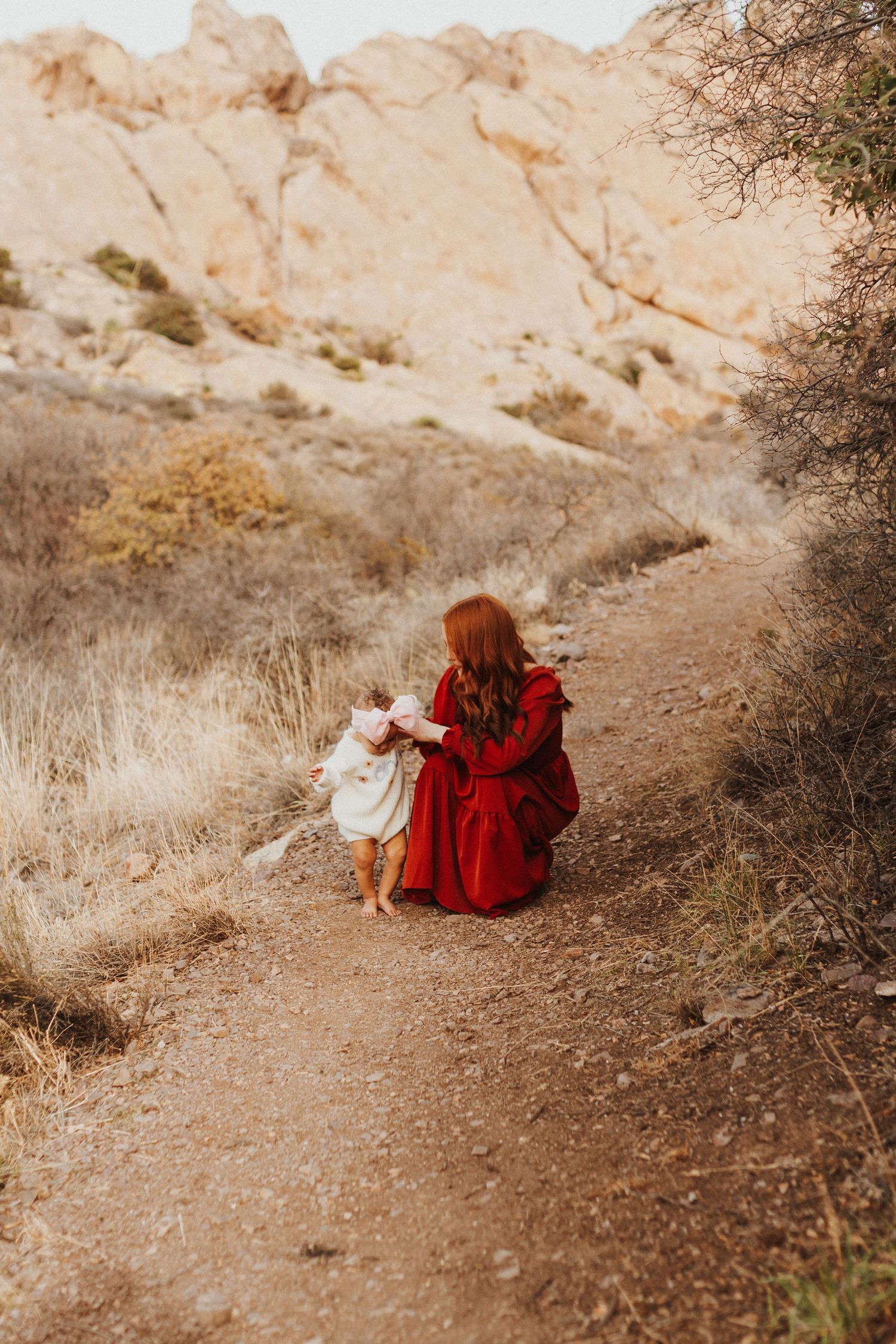 A touching moment between parent and child walking on a desert trail with rocky cliffs in background.