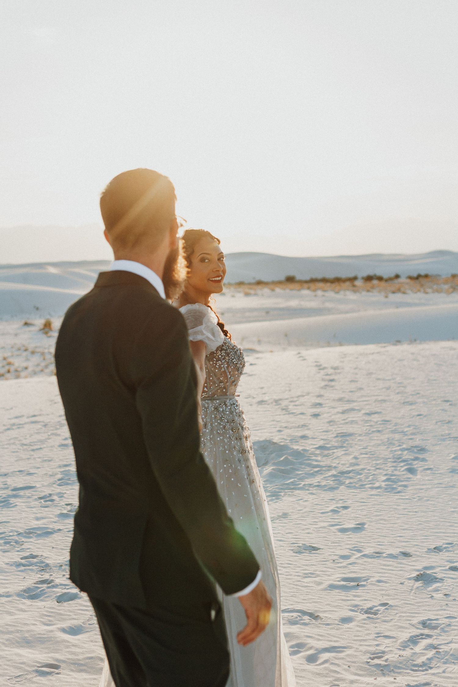 A couple shares an intimate sunset moment on white sand dunes during their wedding day.
