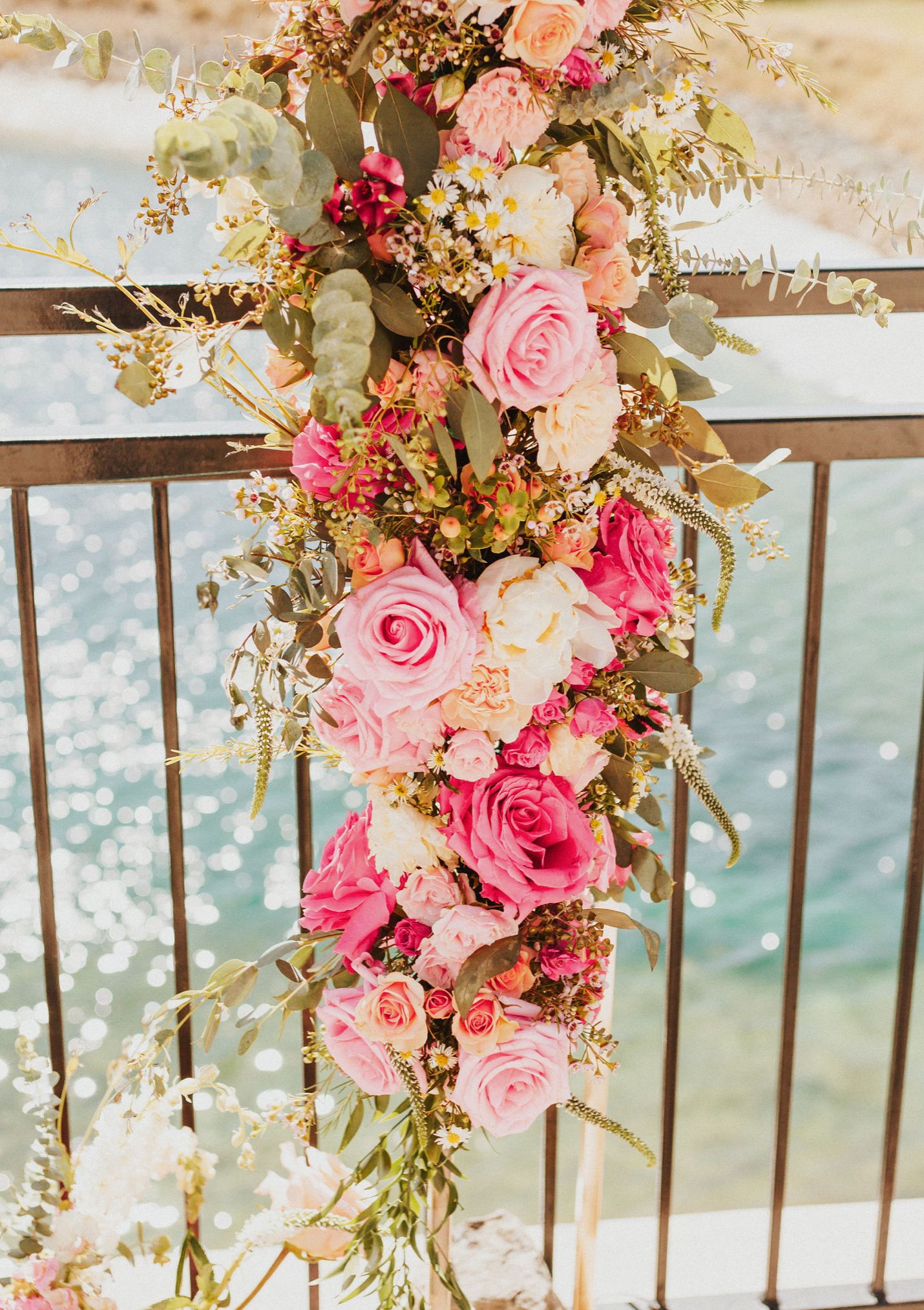 Elegant floral arrangement with pink roses cascading over a waterfront railing.