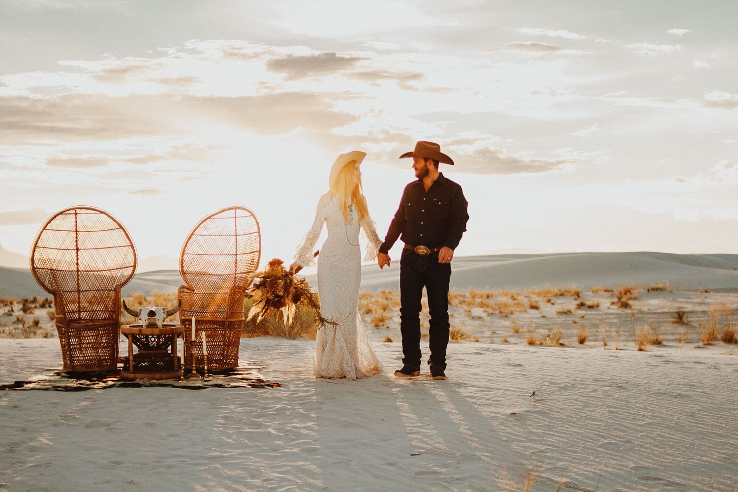 Desert wedding scene with peacock chairs and western-inspired decor at sunset.