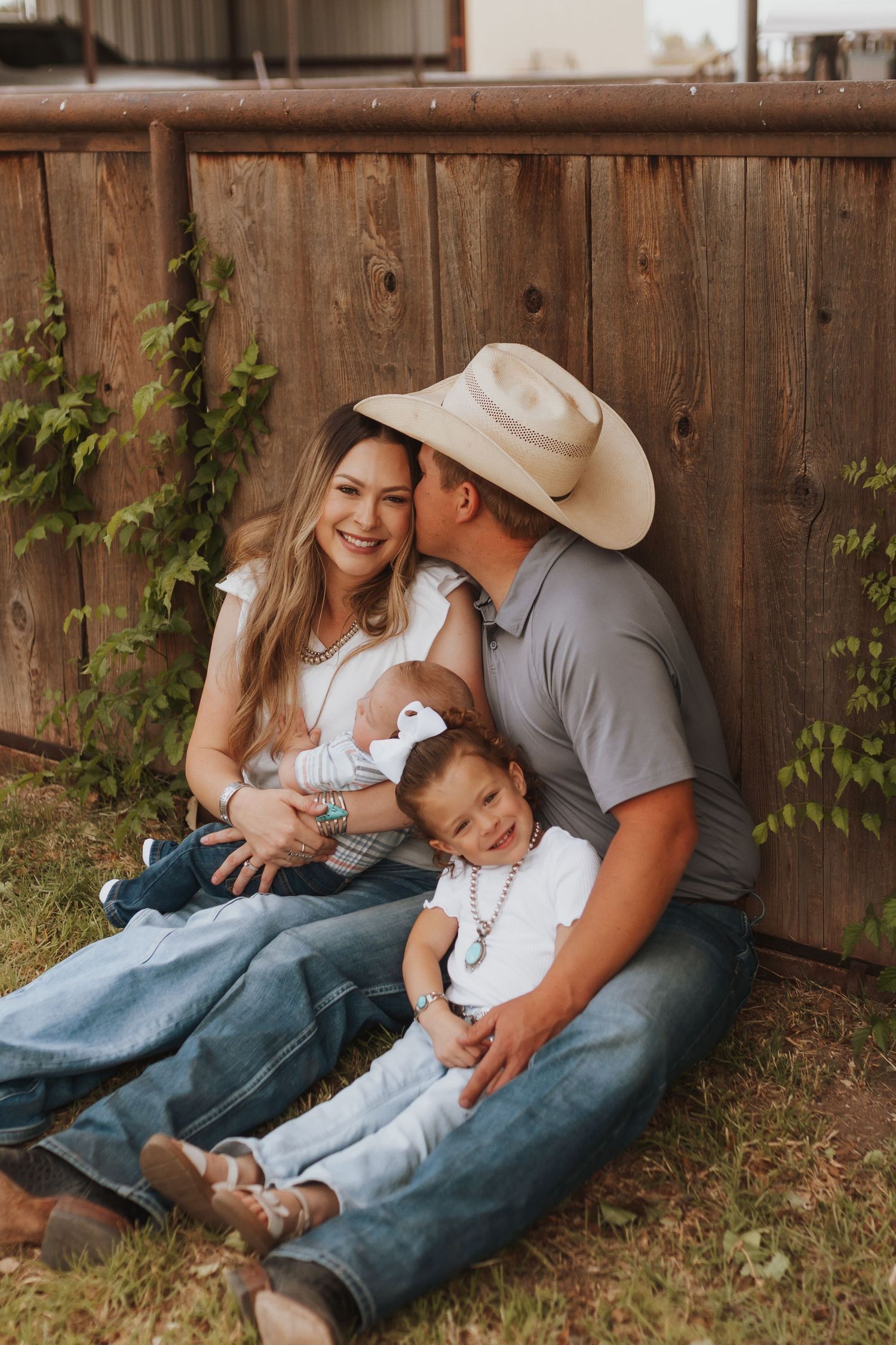 Family sharing intimate moments while lounging against wooden fence outdoors.