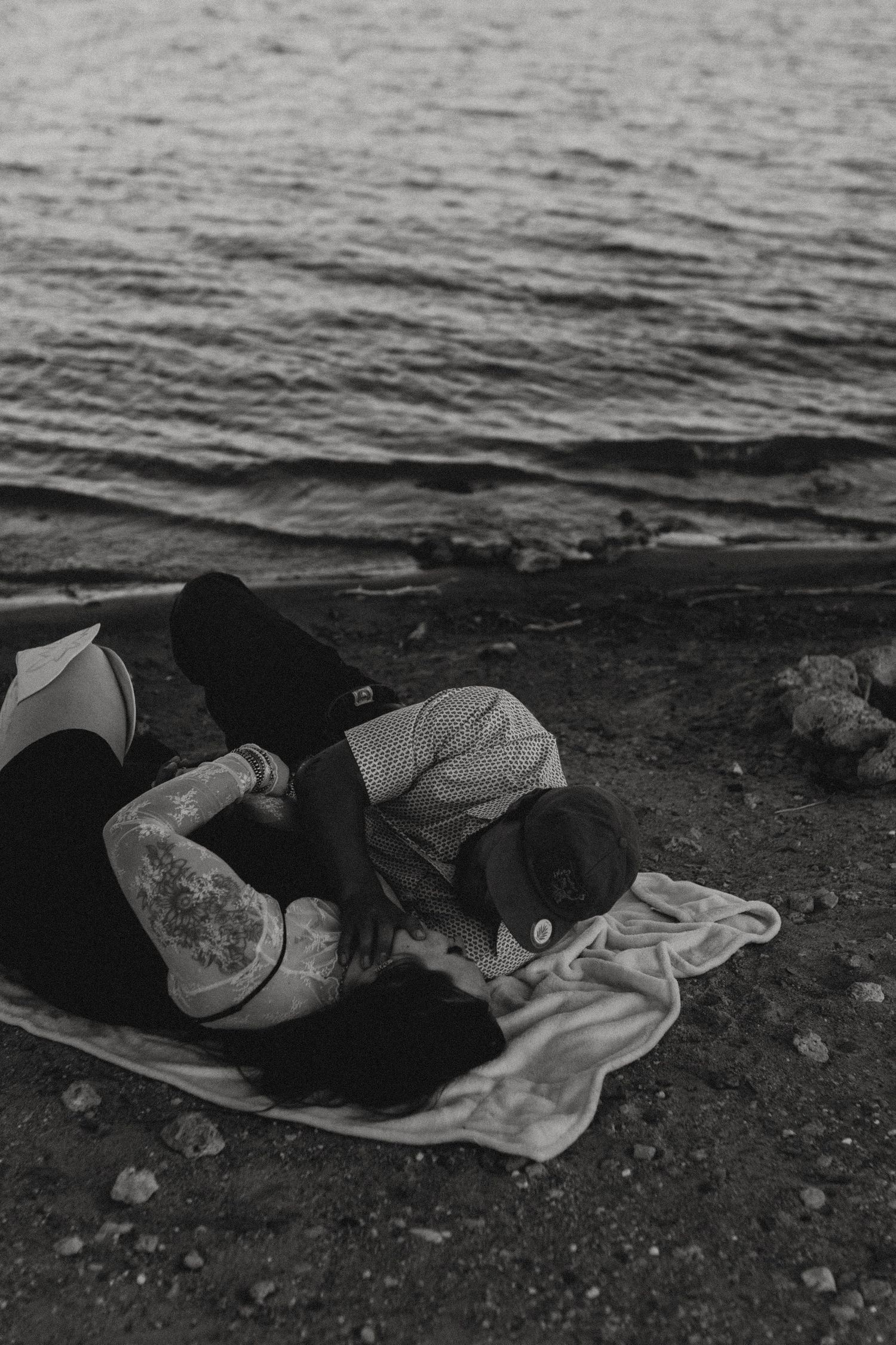 Person resting on a blanket by the water's edge in black and white photography.