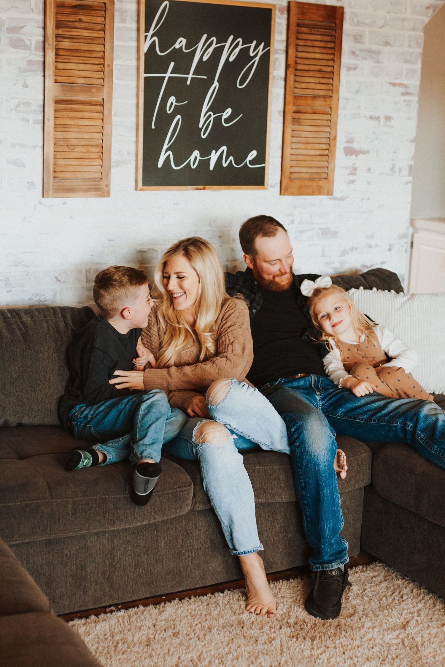 Happy family moment captured on grey couch under decorative wall sign.