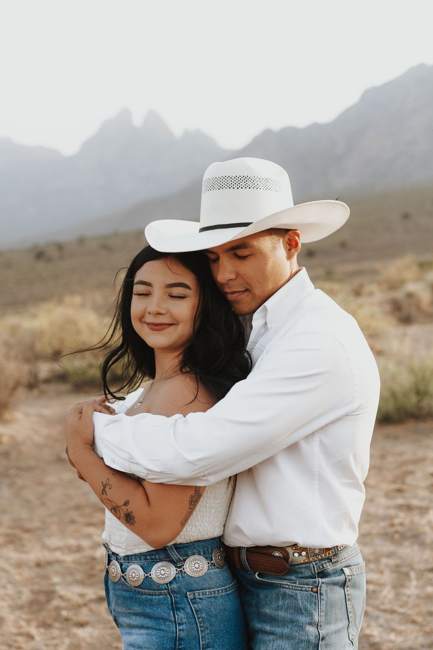 Romantic desert engagement photos featuring western style outfits and cowboy hats.