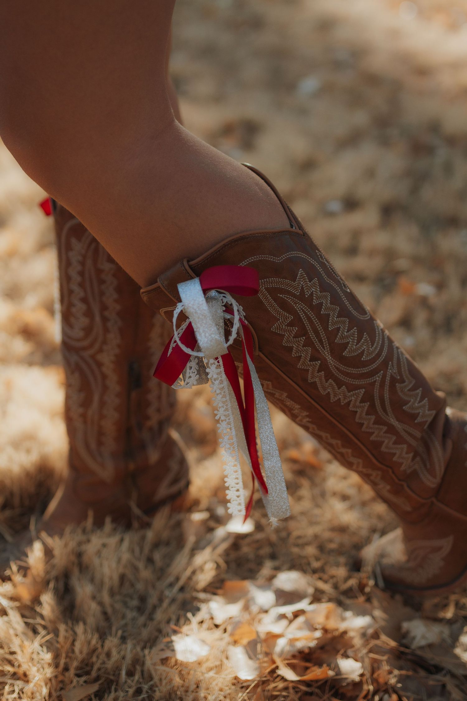 Close-up of decorative brown cowboy boots with red and white ribbons against desert ground.