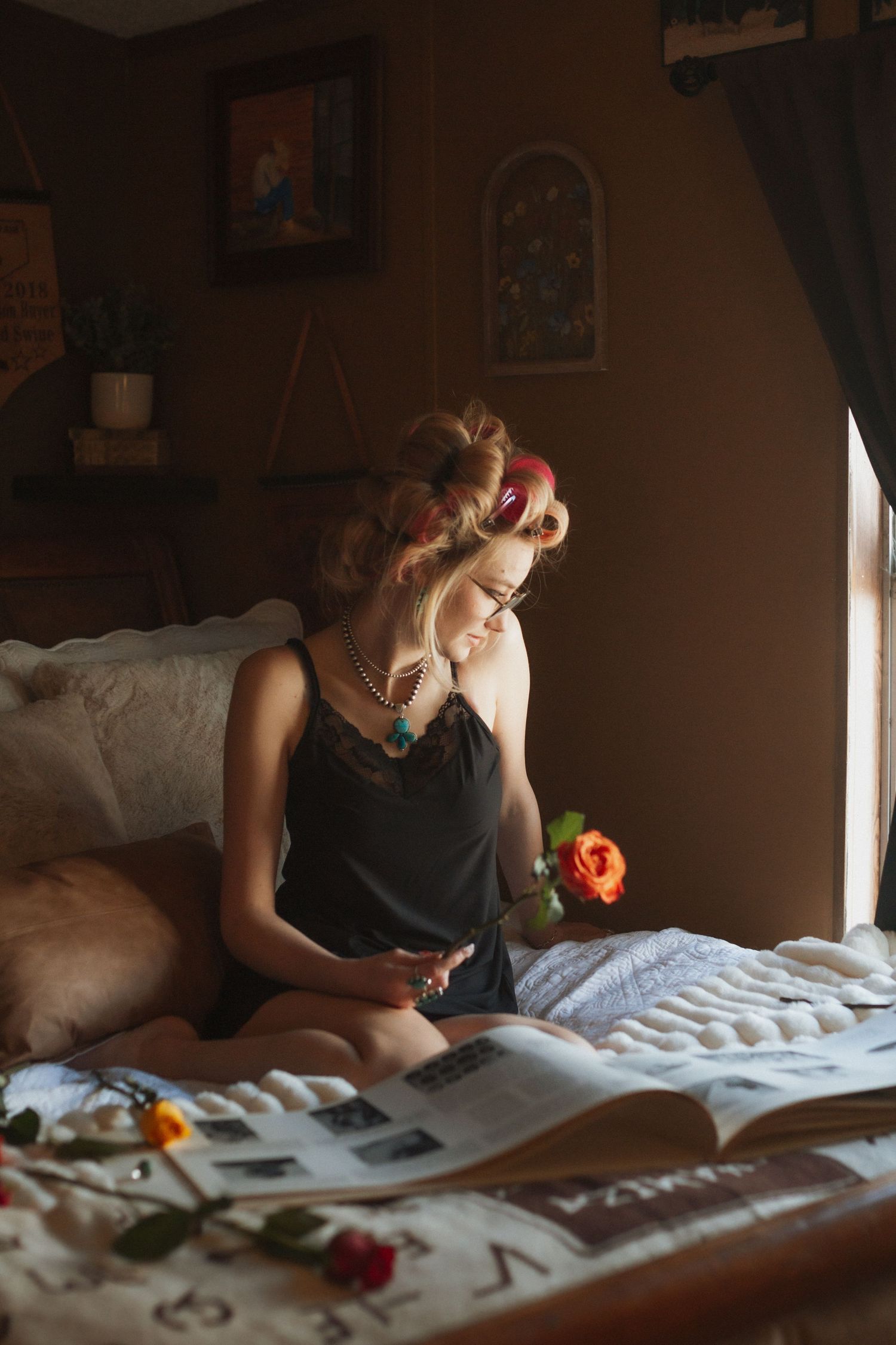 Vintage-style boudoir scene with person reading magazine on bed in warm lighting.