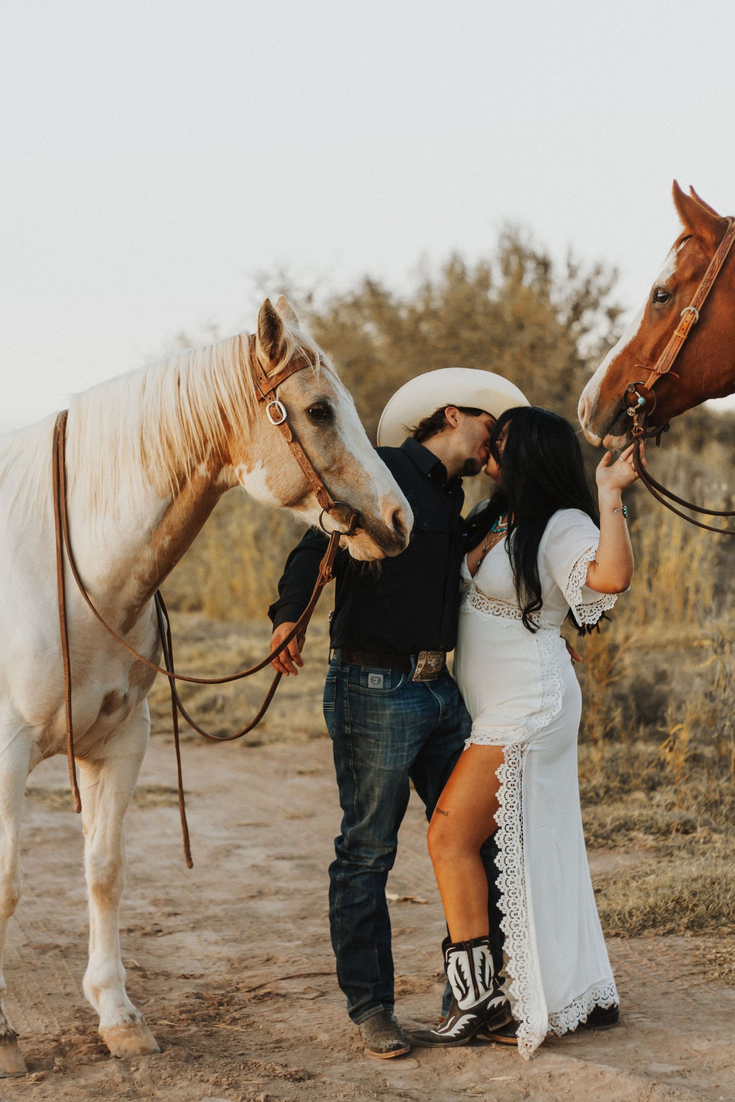 Newlywed couple posing with white horse in desert setting.
