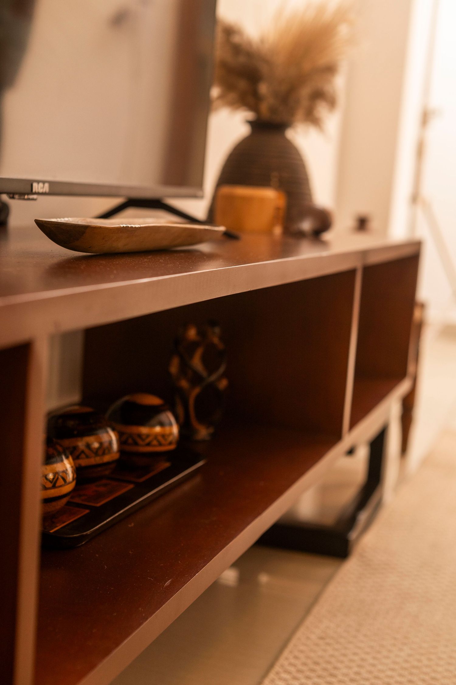 Modern wooden storage unit with dried flowers in vase and decorative items on display.