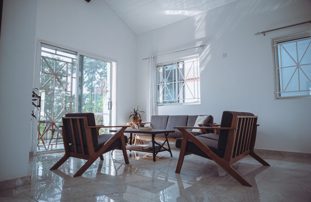 Sunlit living room with wooden furniture, grey sofa, and multiple geometric windows.