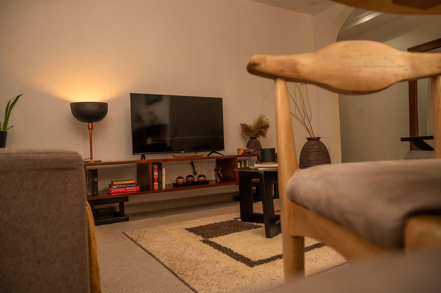 Modern living room with TV setup, gray couch, and wooden furniture in warm lighting.