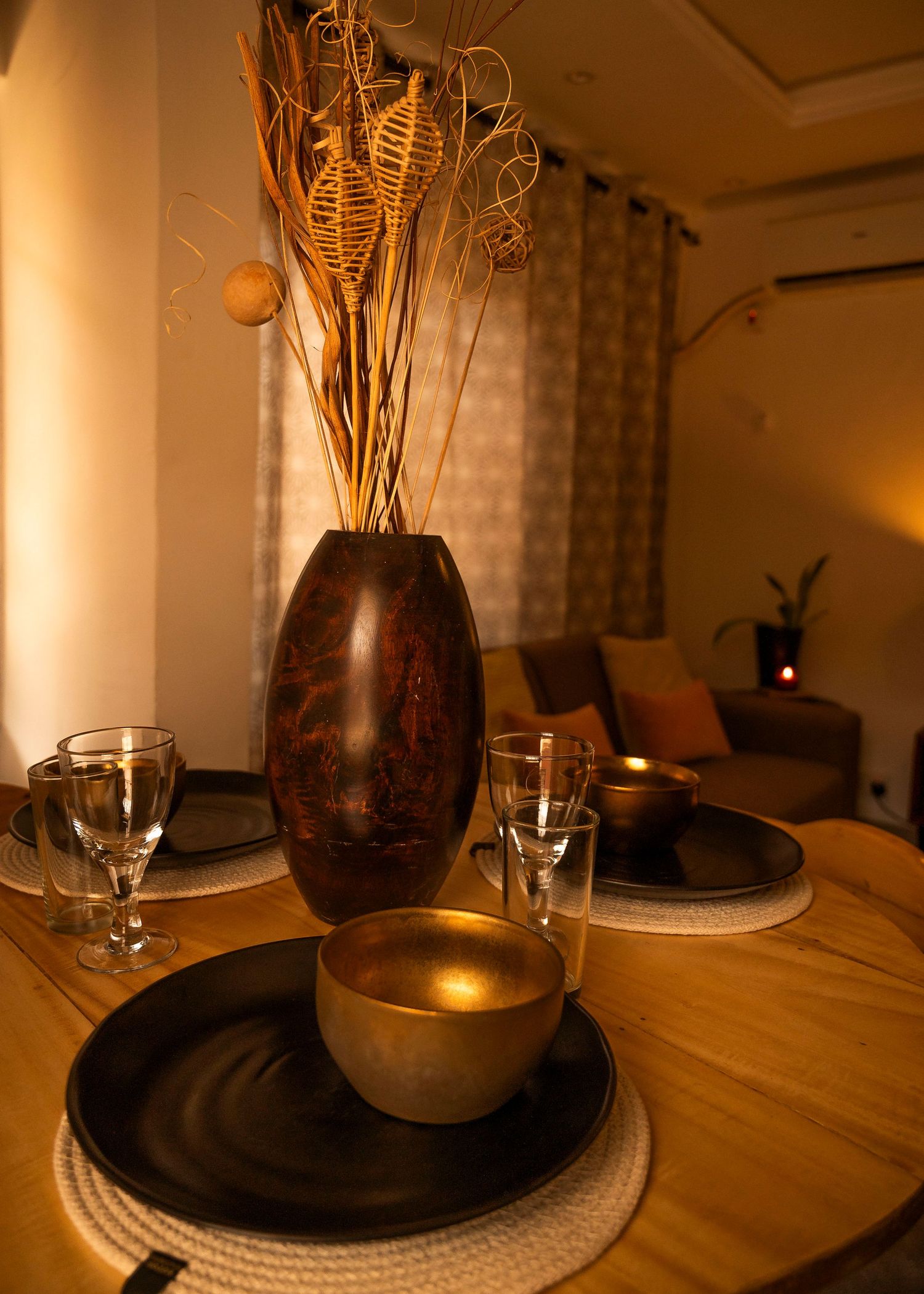 Decorative vase with dried plants on a wooden table with ambient lighting.