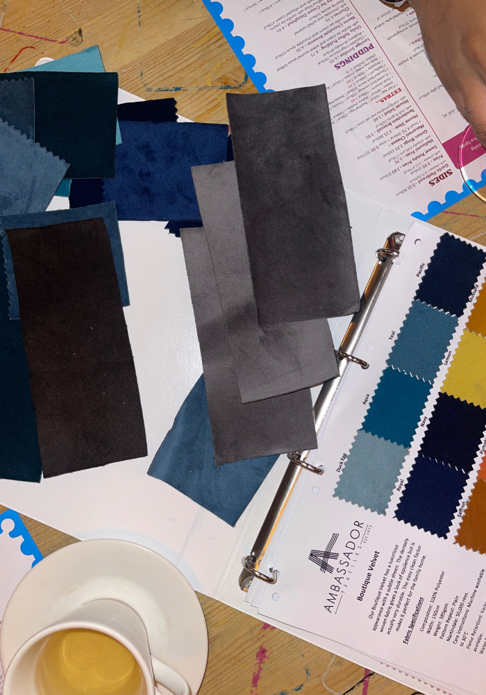 Interior design materials including fabric swatches, color samples and a cup of coffee on a wooden surface.