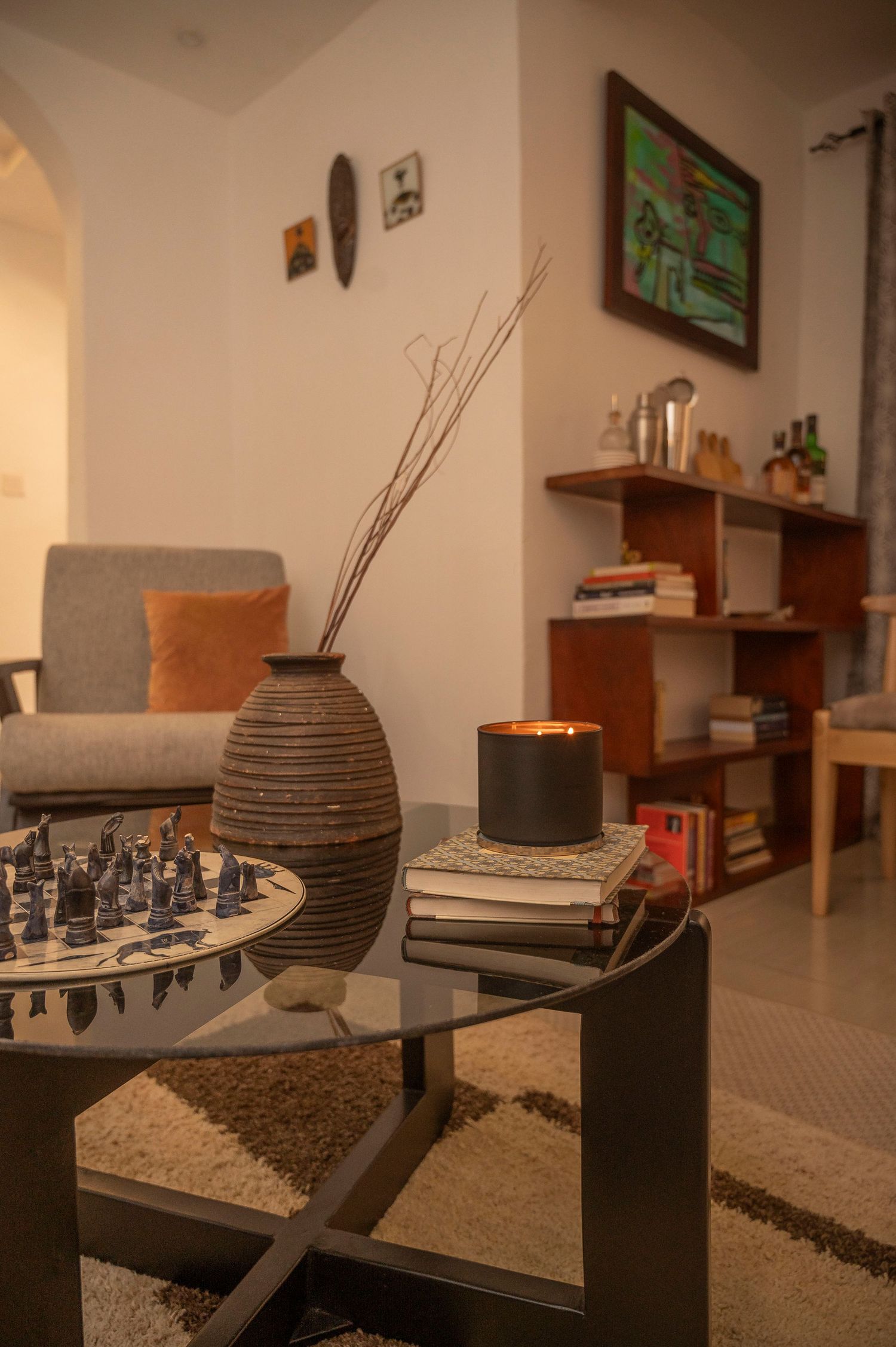 Chess set and textured vase on black coffee table with grey sofa and wall shelving in background.