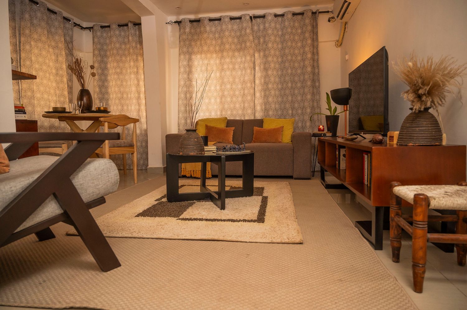 Modern living room with grey sofa, yellow accent pillows, and natural decor elements on a beige area rug.