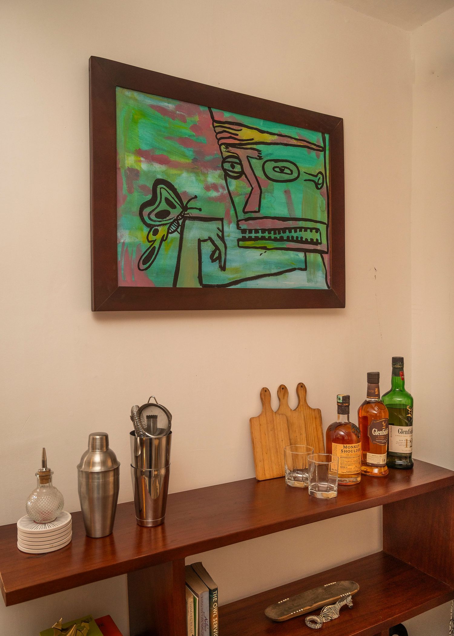 Modern bar setup with colorful abstract art, wooden cutting boards, and various liquor bottles.