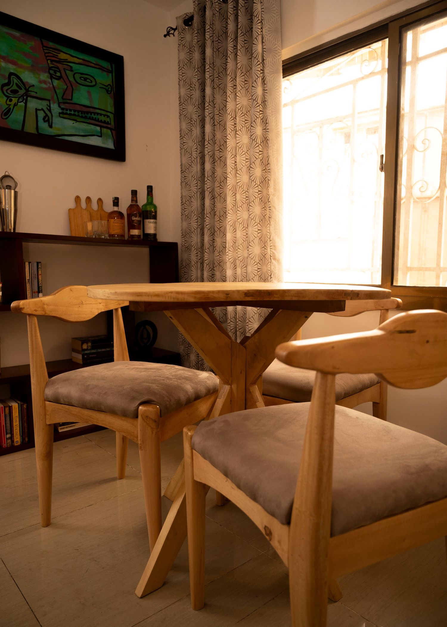 Mid-century modern dining area with wooden chairs and table near a window with patterned curtains.