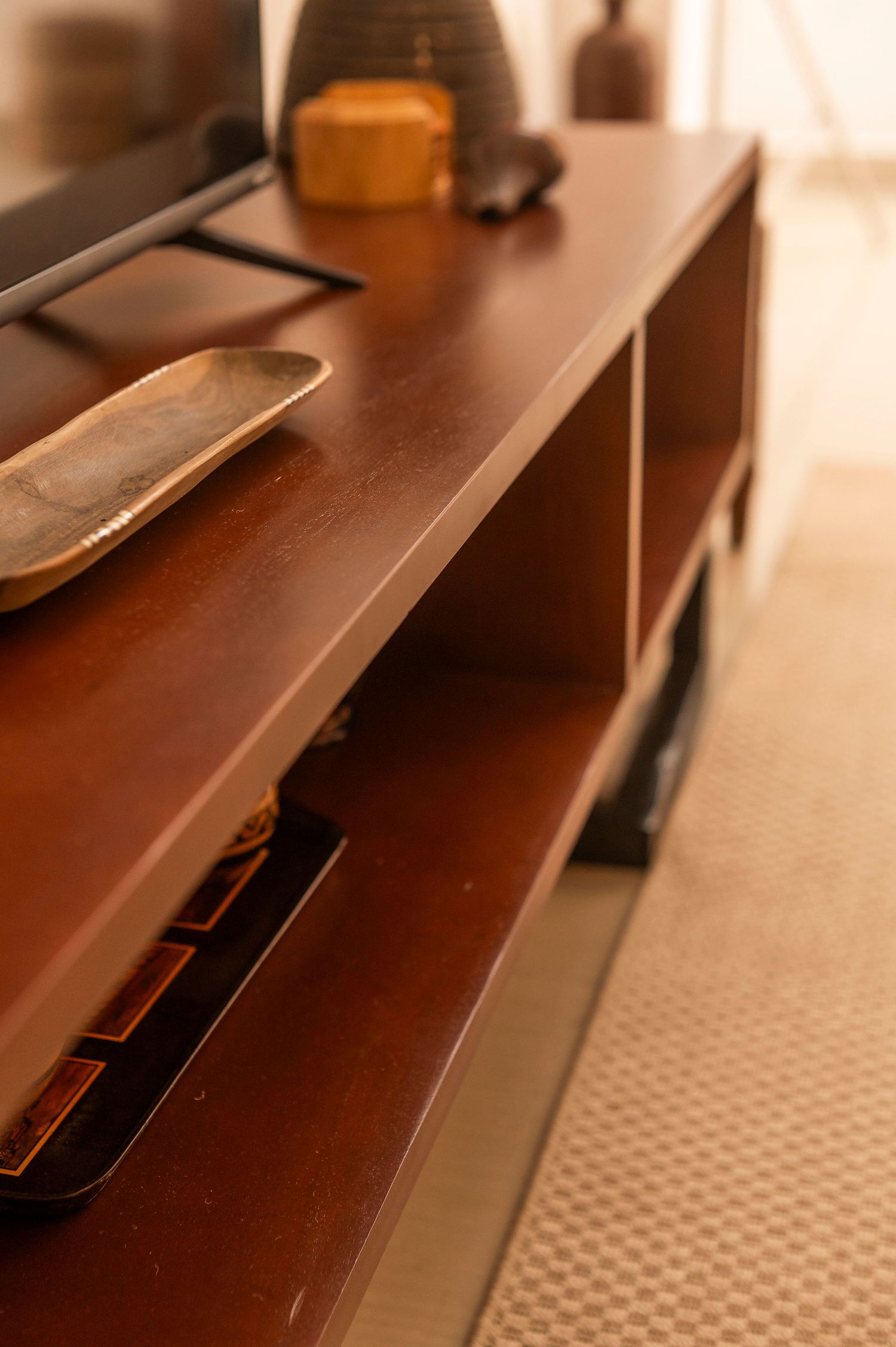 Close-up view of a dark wooden shelf with decorative items and storage compartments in warm lighting.