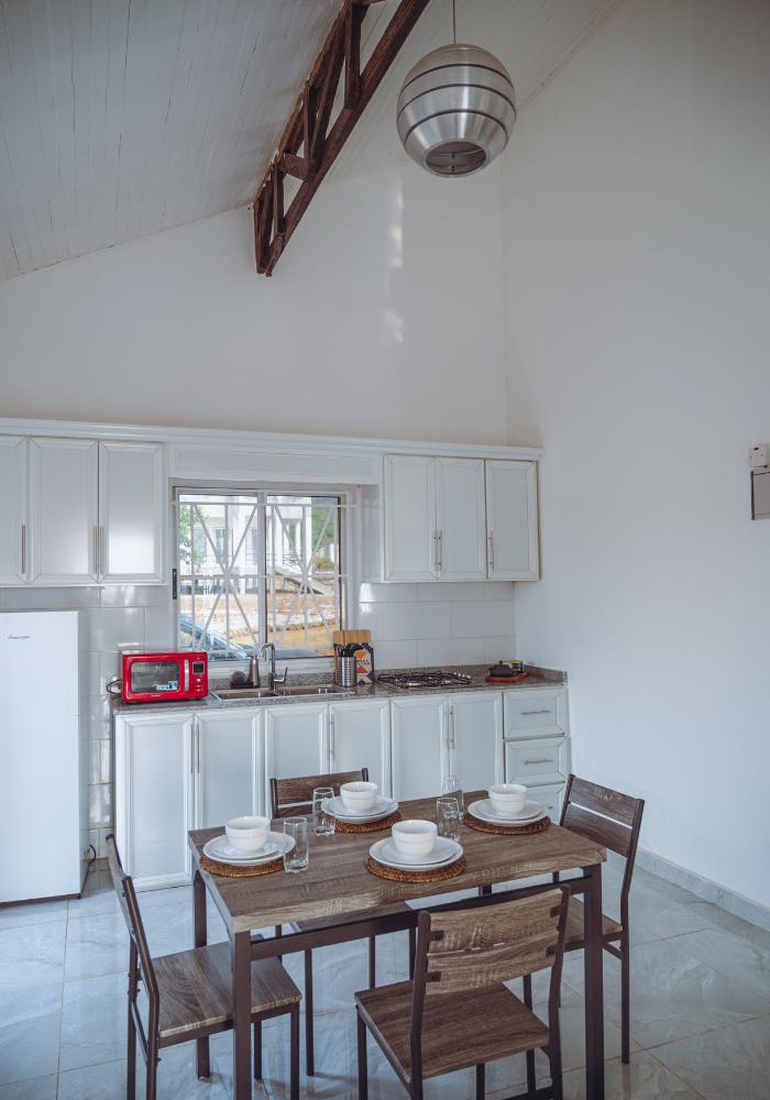 White kitchen with dining set featuring wooden table and chairs under vaulted ceiling with exposed beam.
