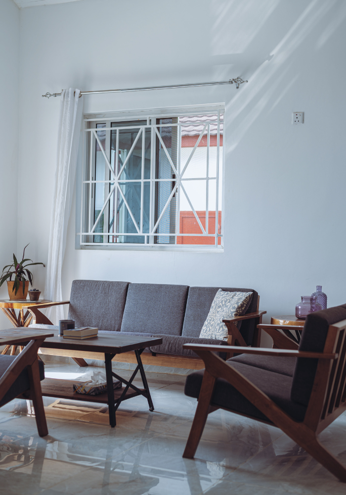 Living room with gray sofa and wooden armchairs near window with decorative metal grille.
