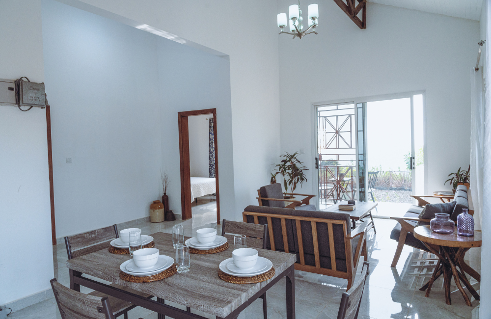 Open concept dining room with white walls, wooden furniture and exposed ceiling beam.