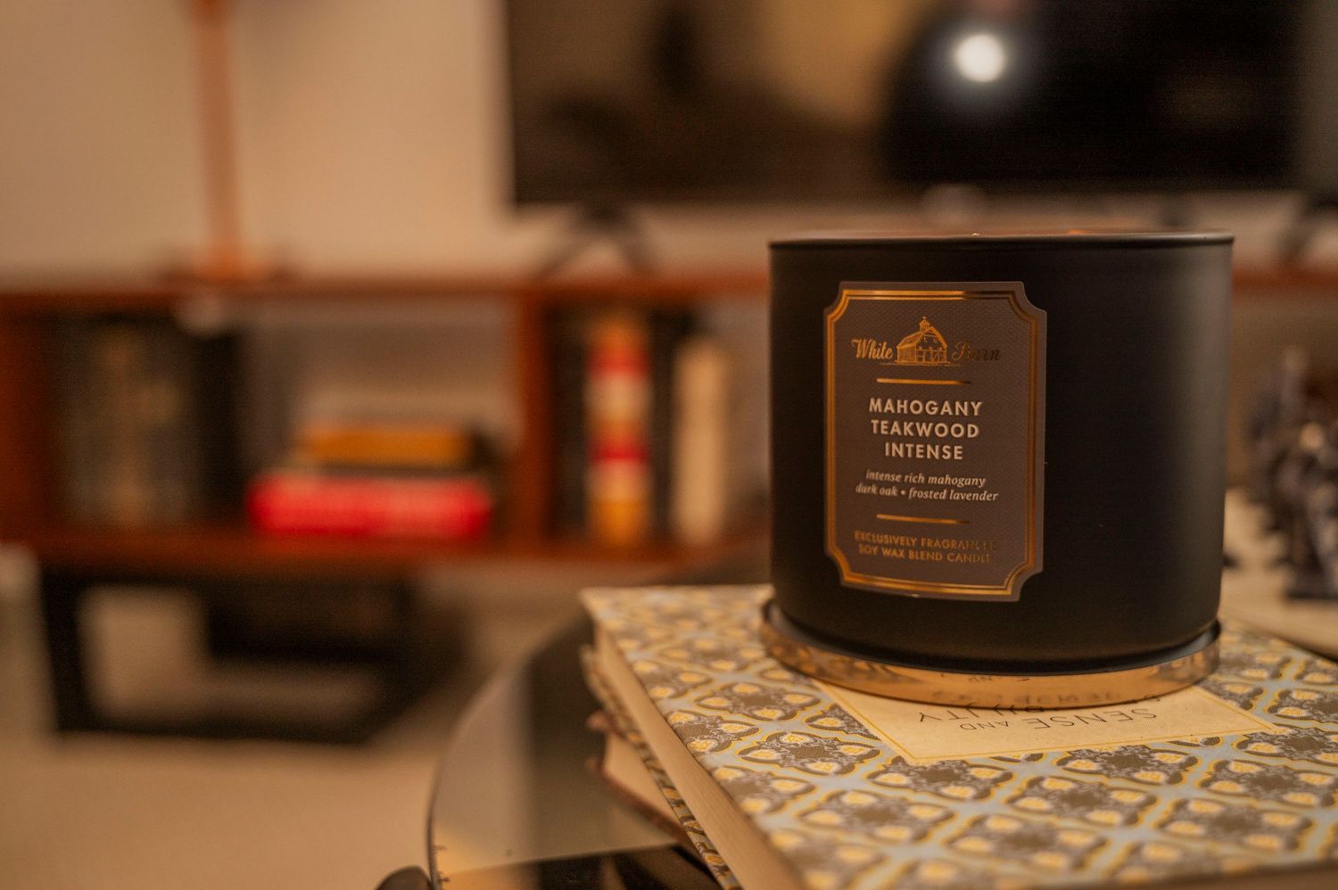 Black scented candle on patterned coaster with blurred background interior.