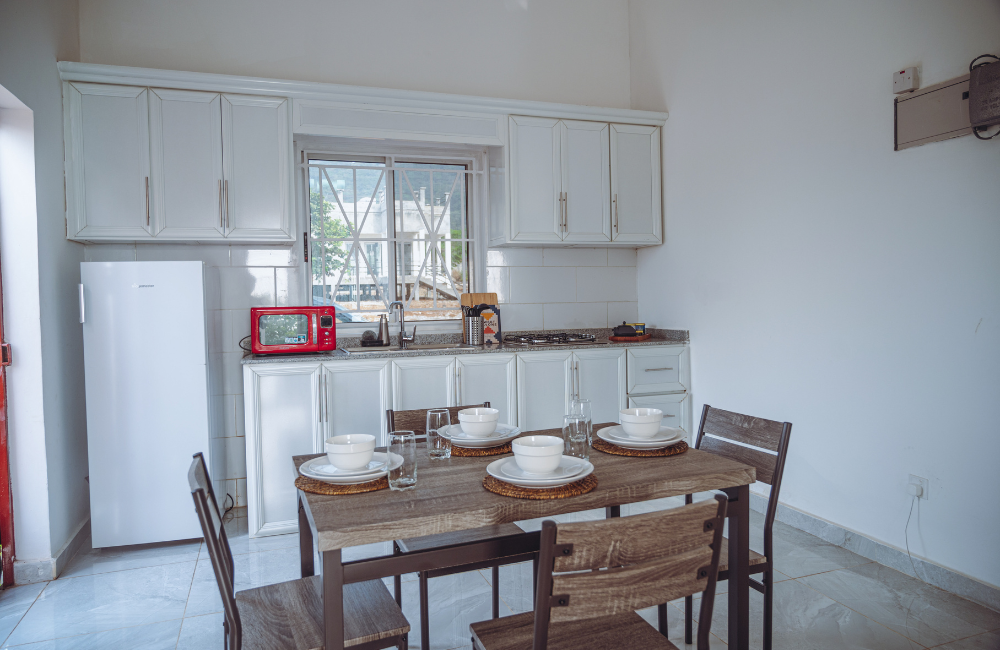Modern white kitchen with wooden dining table and chairs featuring minimal decor and bright natural lighting.