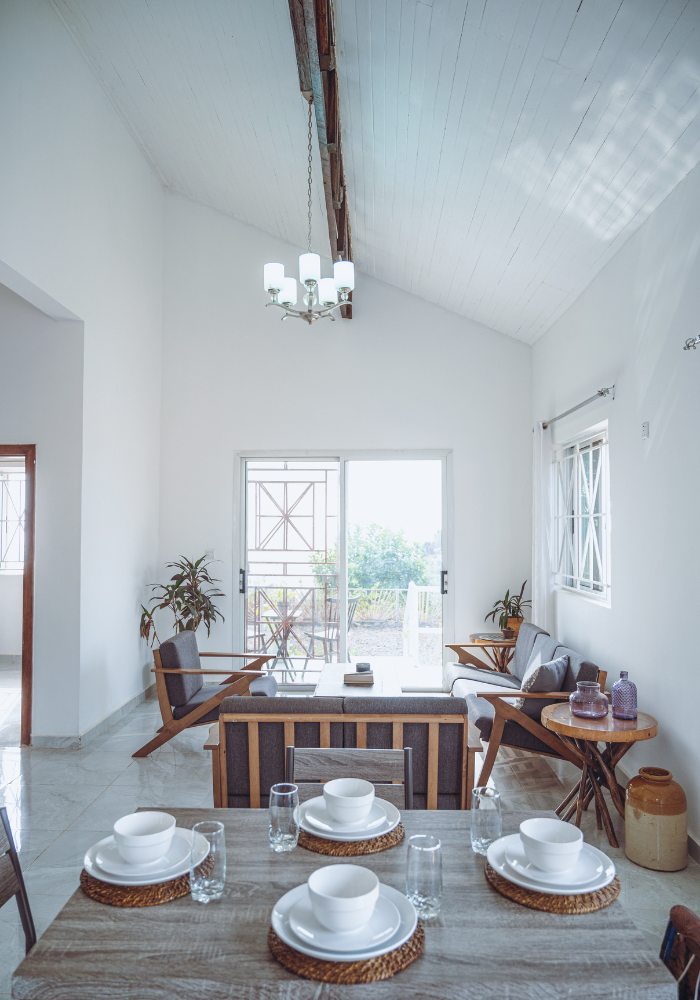 Bright dining space with wooden table set for four and mid-century modern furniture under vaulted ceiling.