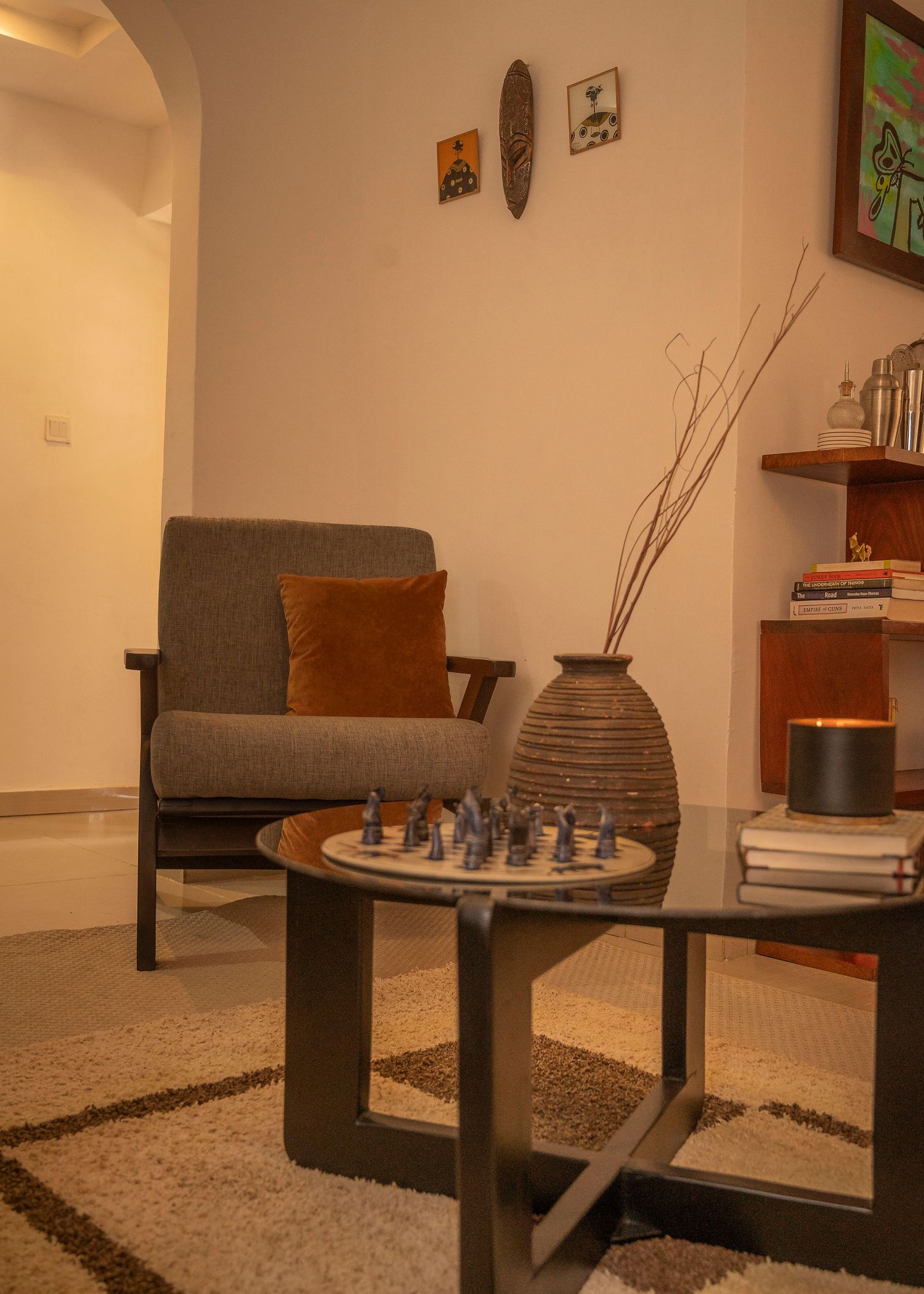 Contemporary living space with chess set on coffee table and textured grey armchair with orange cushion.