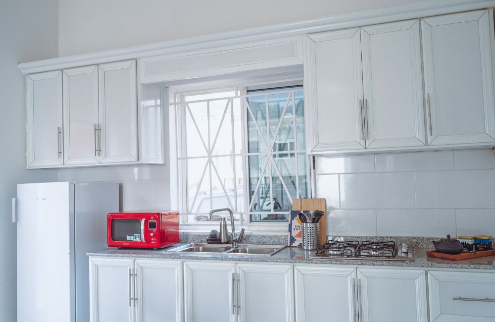 White kitchen with red microwave, stainless appliances and window with geometric metal grille.
