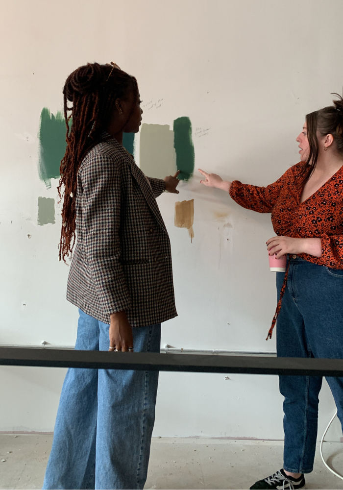 Two people discussing while looking at partially painted wall samples.