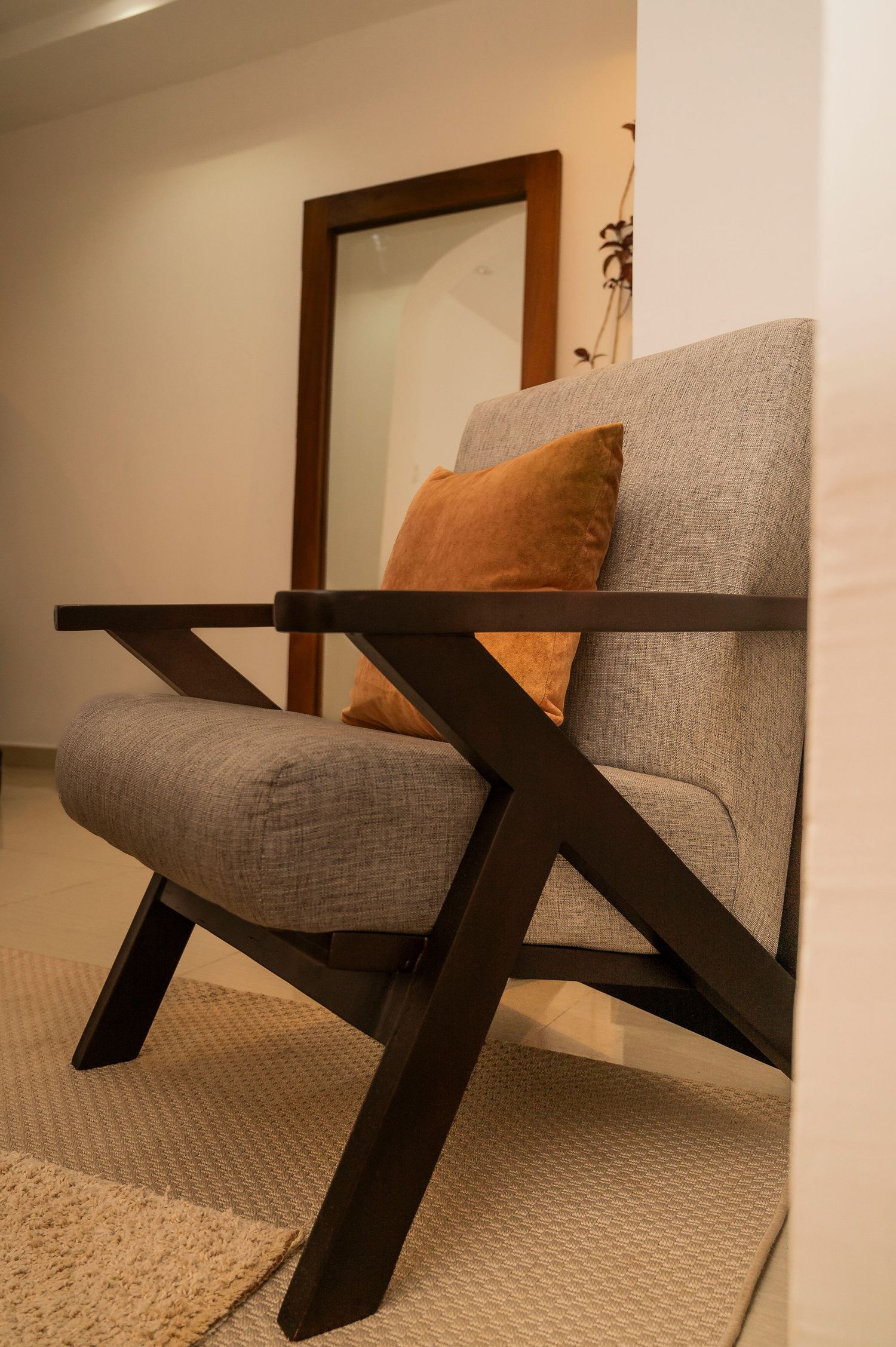 Gray upholstered lounge chair with modern X-frame legs on carpet.