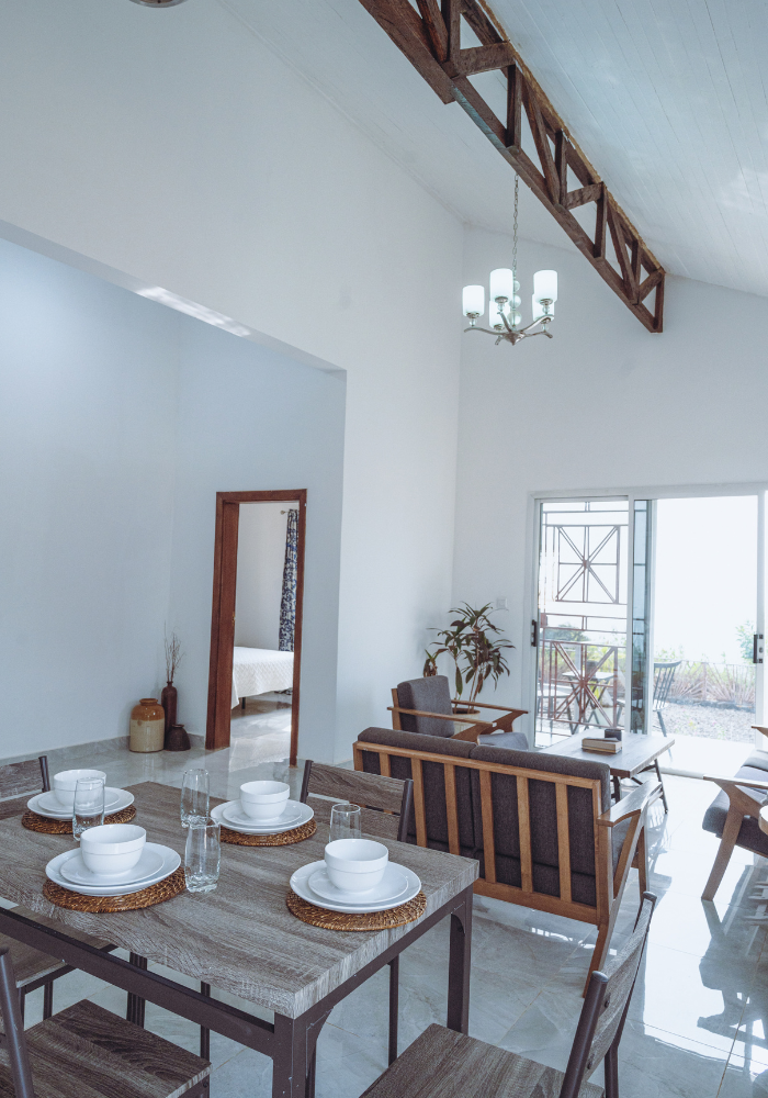Dining area with wooden table and chairs under exposed beam ceiling and chandelier lighting.