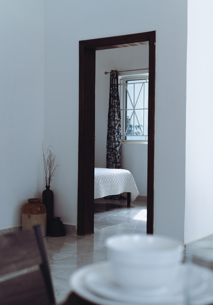 View through doorway into bright bedroom with floral curtains and white bedding.