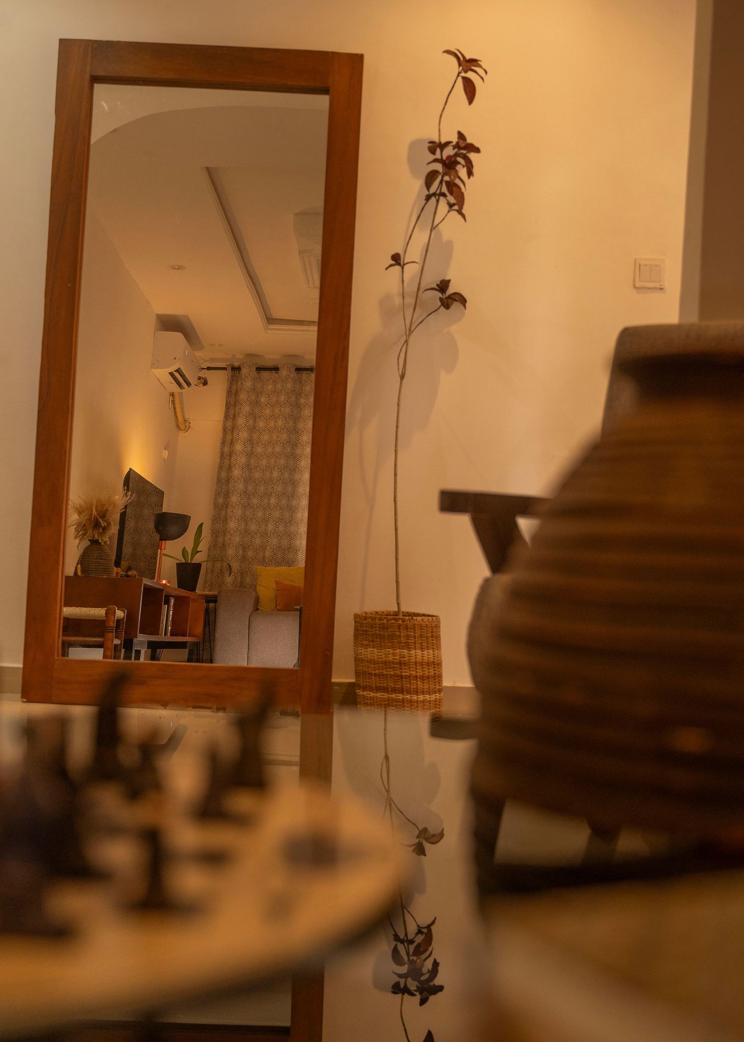 Tall wooden framed mirror reflecting room interior with decorative branches and ceramic vase.