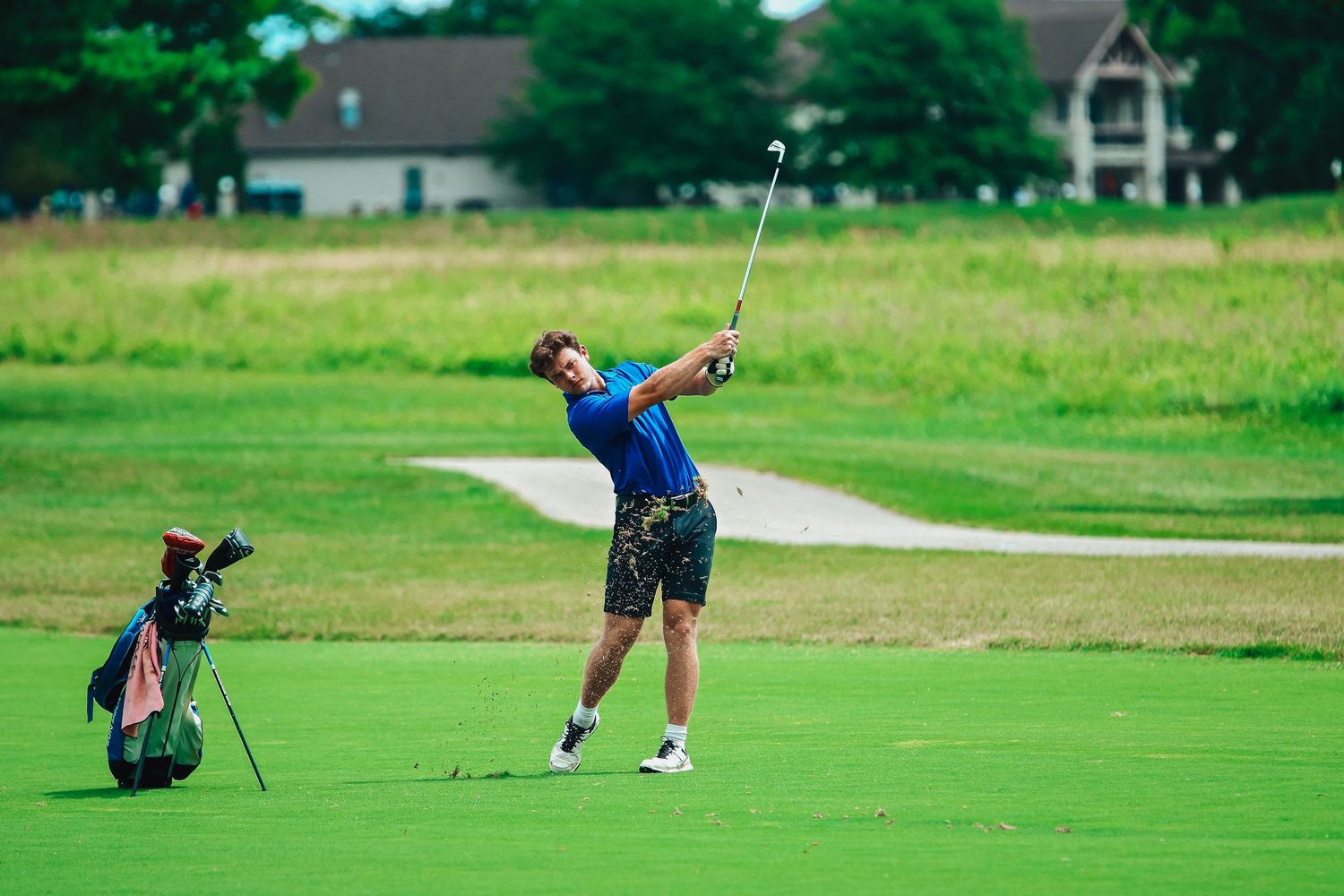 Golfer wearing blue mid iron swing in the fairway
