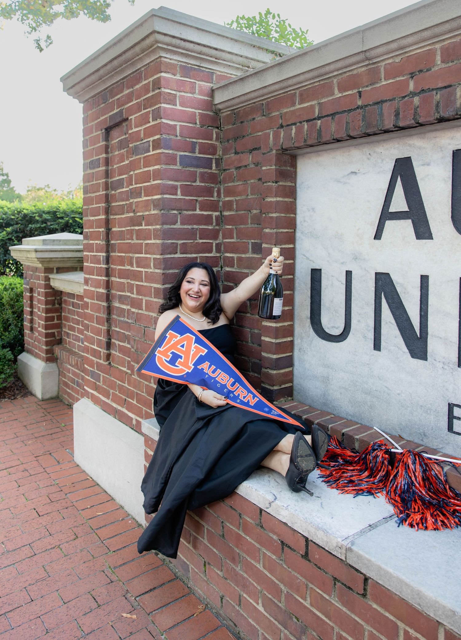 A person holding a university pennant poses by a brick entrance wall.