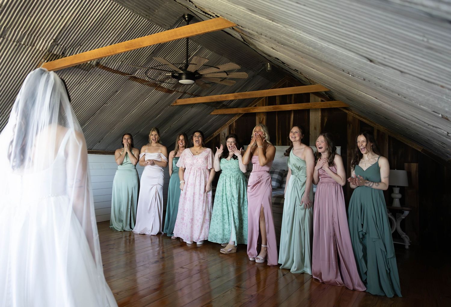 Wedding party in pastel dresses gathered in rustic barn setting.