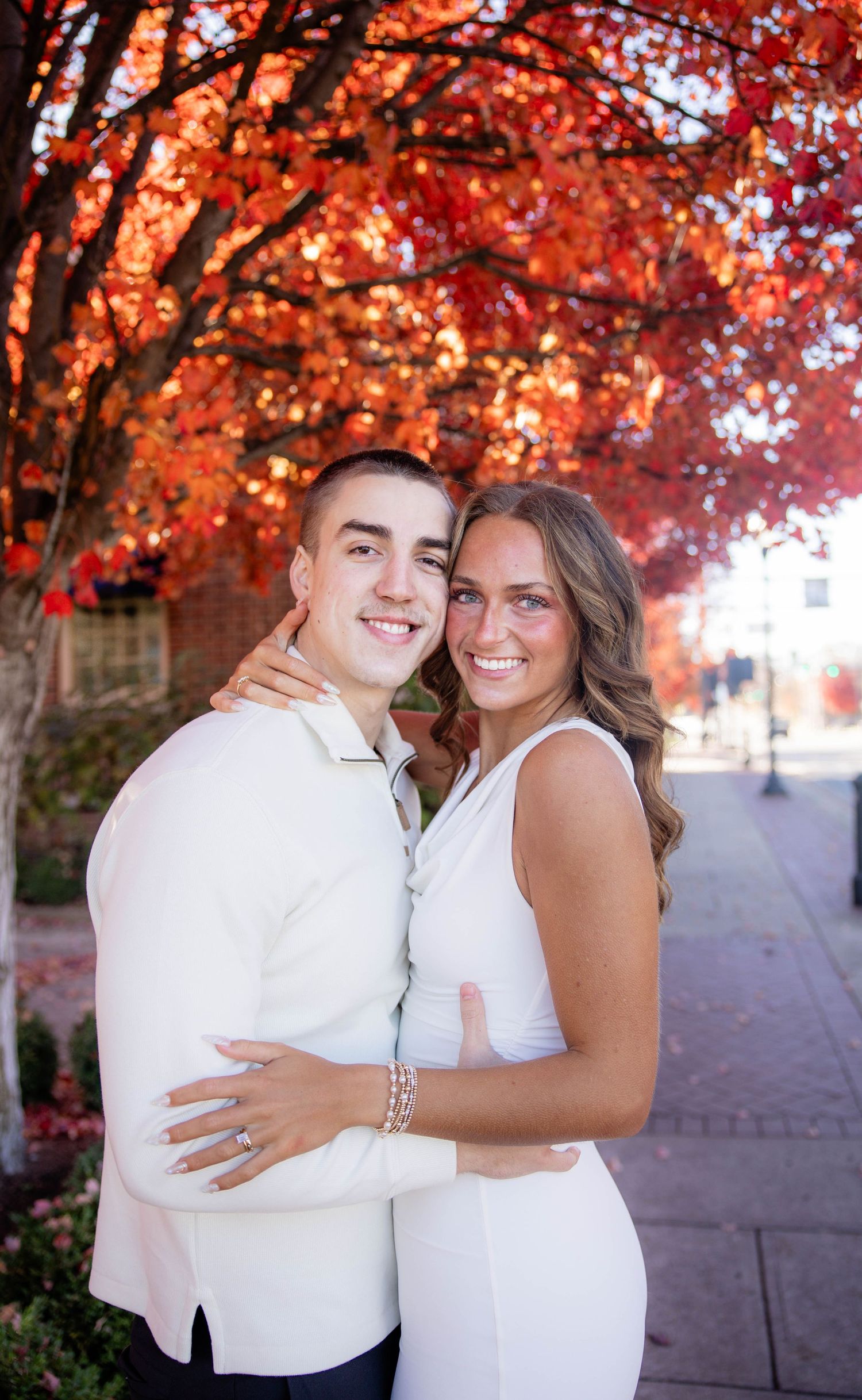 A couple shares romantic moments under vibrant red autumn trees during a wedding photoshoot.