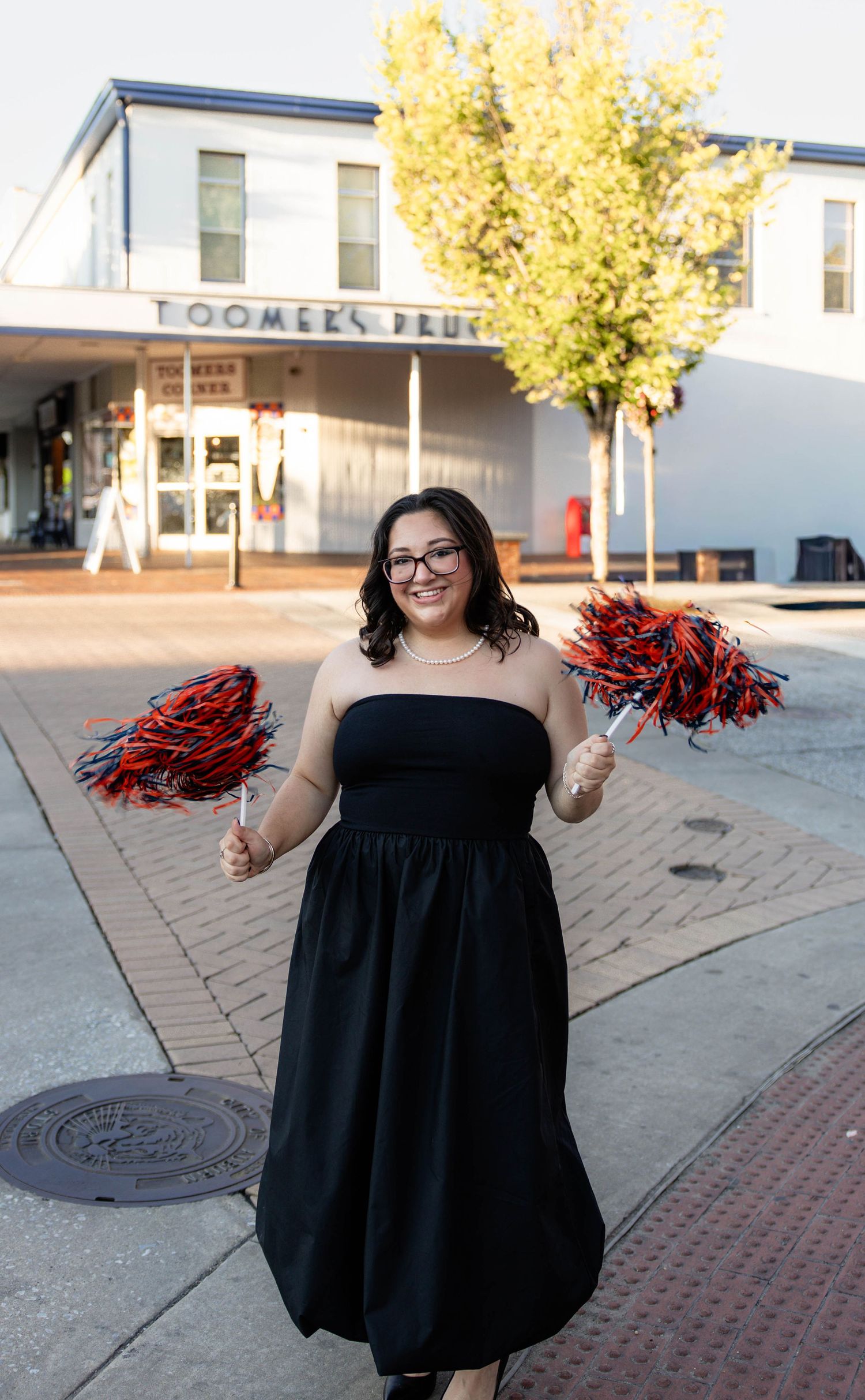 A person in a black dress holds red pom poms outside a building.