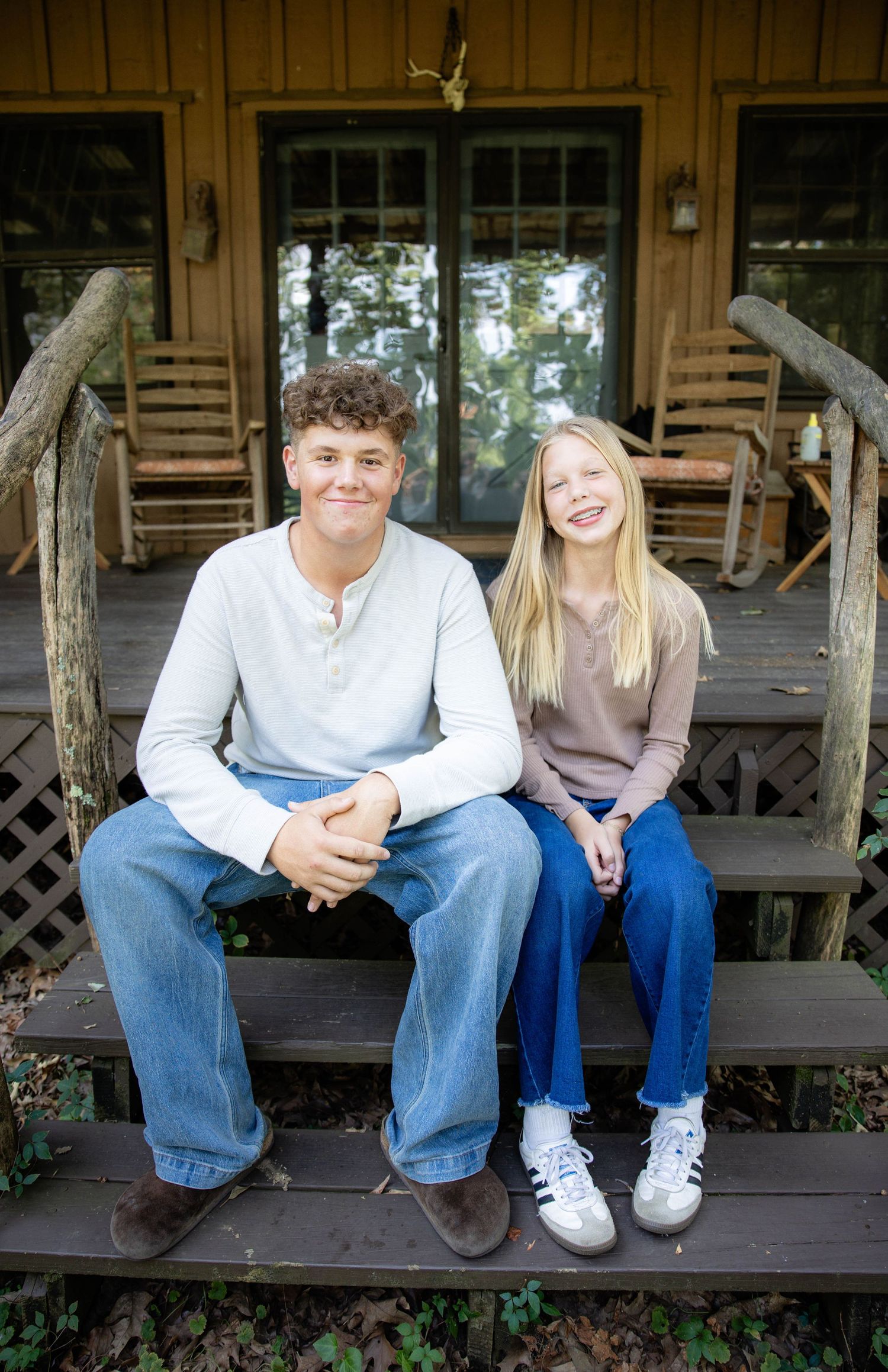 Two people sit casually on wooden porch steps of a cabin.