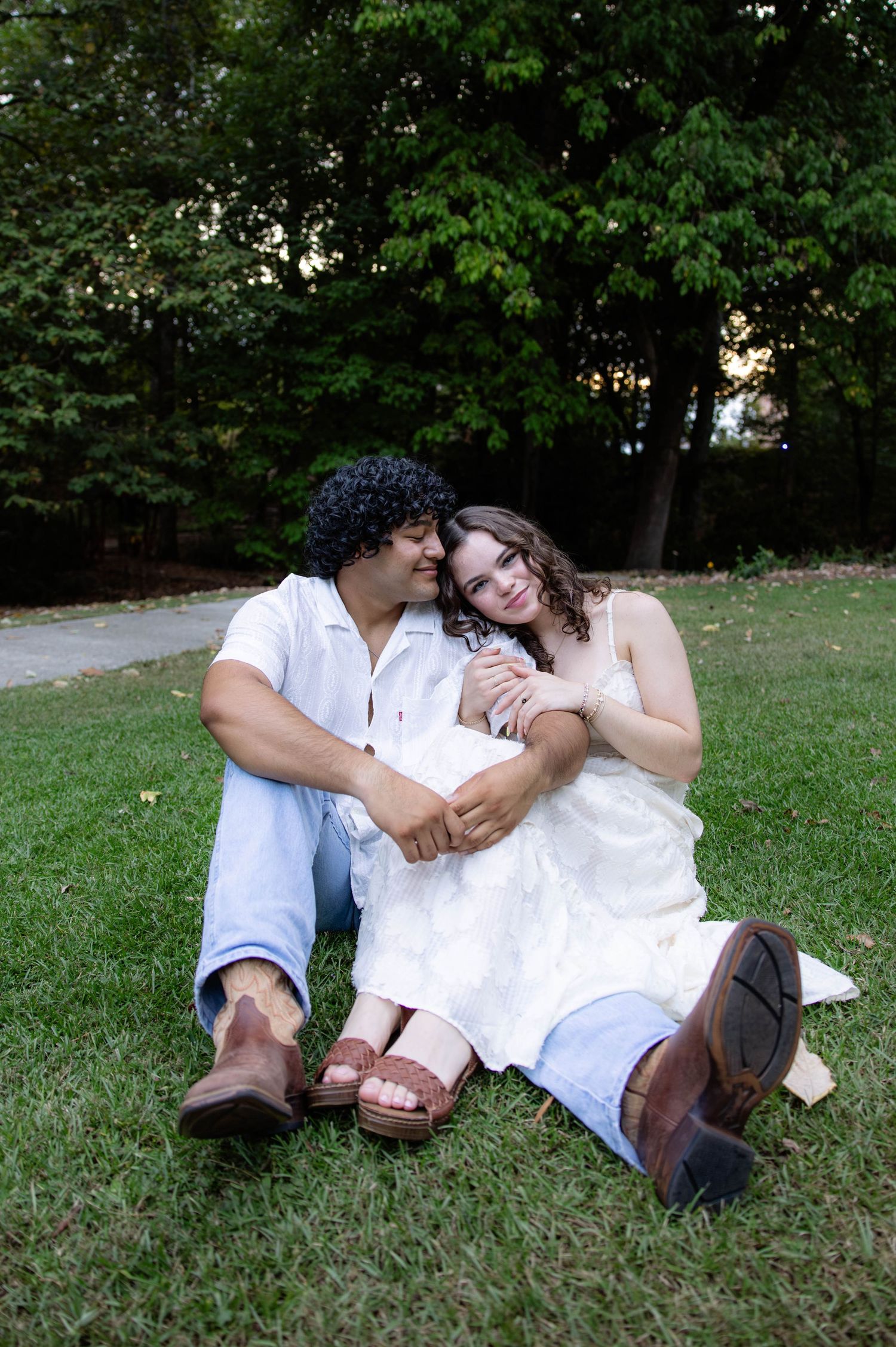 Couple in white outfits shares playful moments while sitting together on grass.