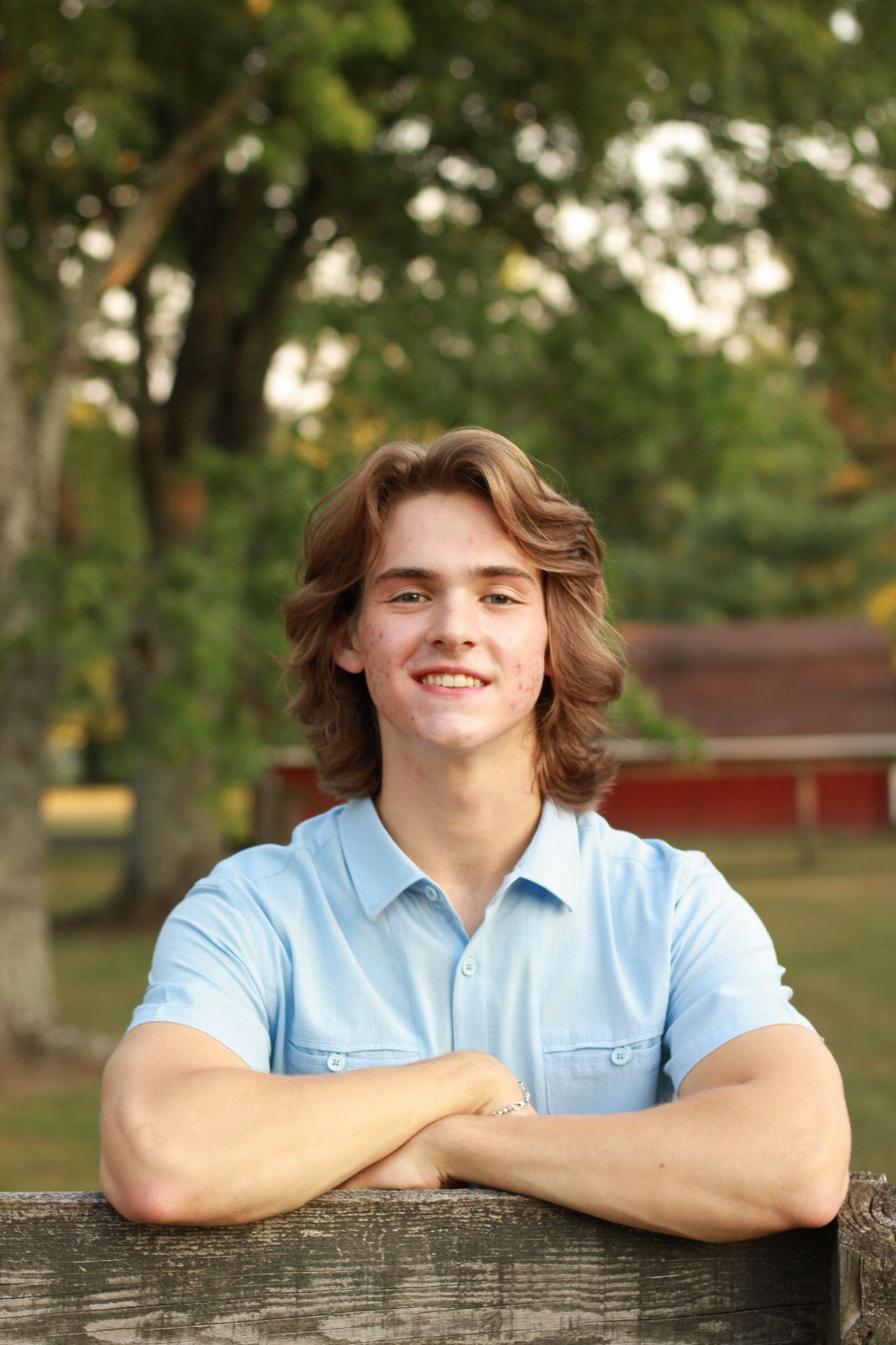 Portrait series of someone in a light blue polo shirt leaning on a wooden fence outdoors.