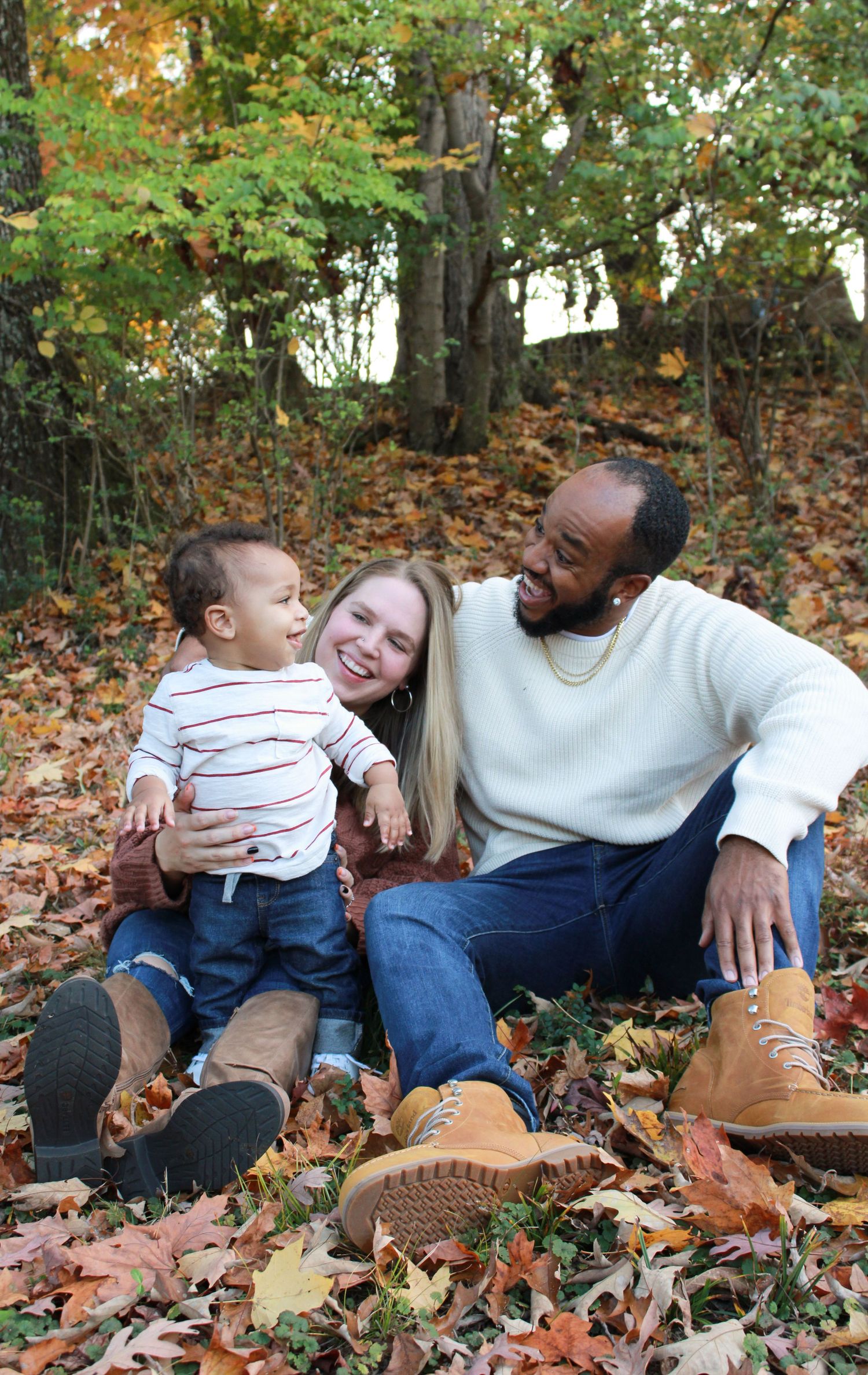 Family relaxing together on fallen autumn leaves in outdoor setting.