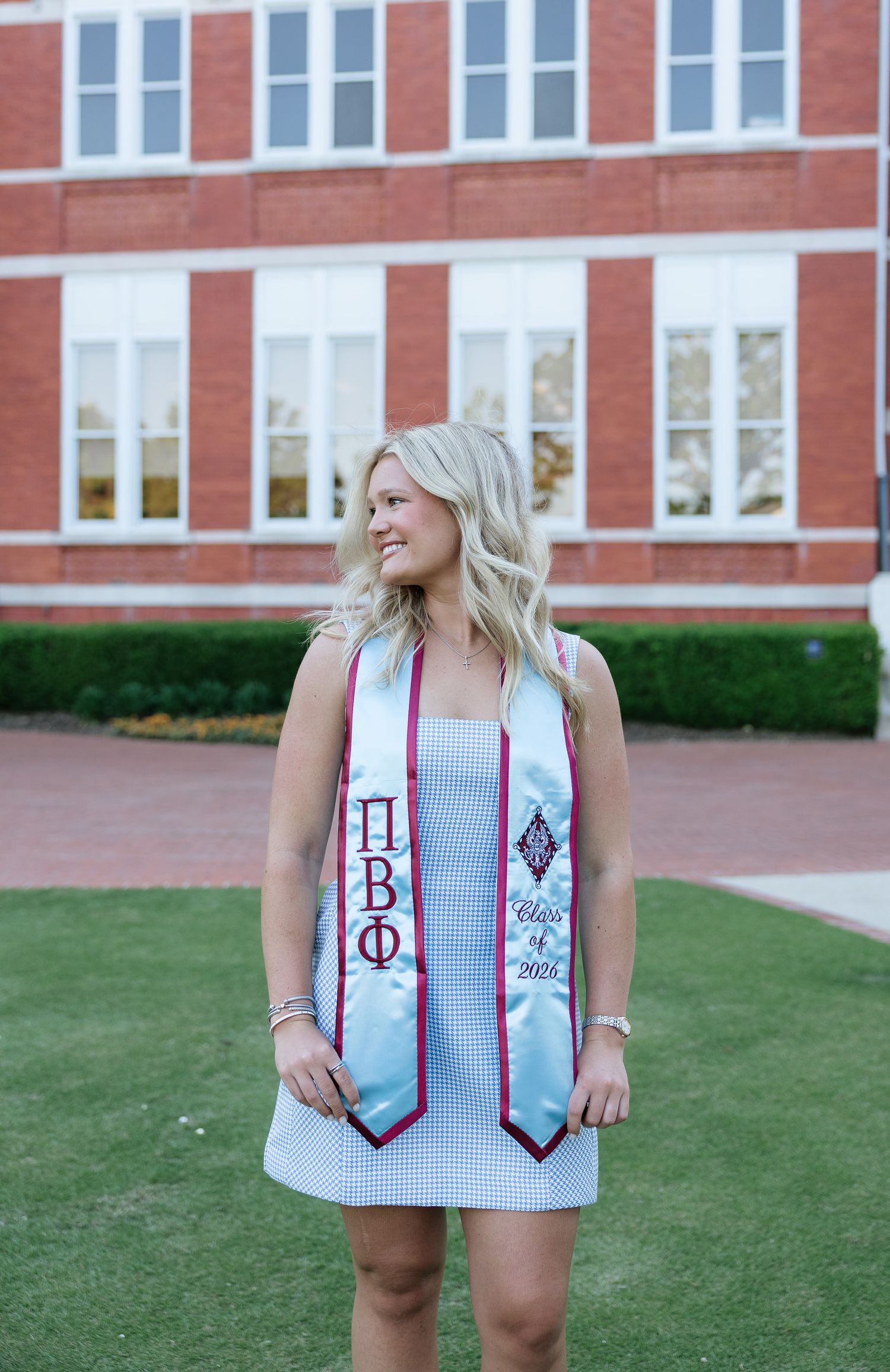 Blonde woman wearing Pi Beta Phi graduation stole over blue dress, posing outdoors near brick building, Class of 2021.