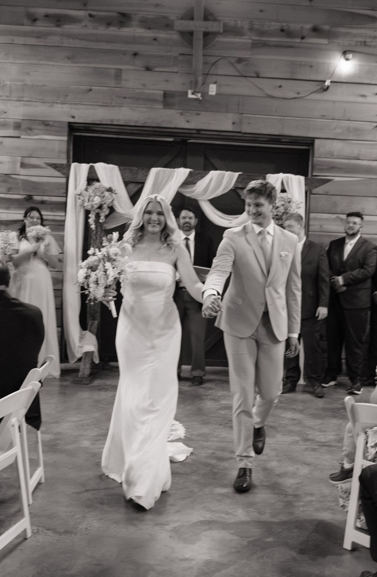 Bride and groom walk down the aisle hand in hand after wedding ceremony in rustic barn venue.