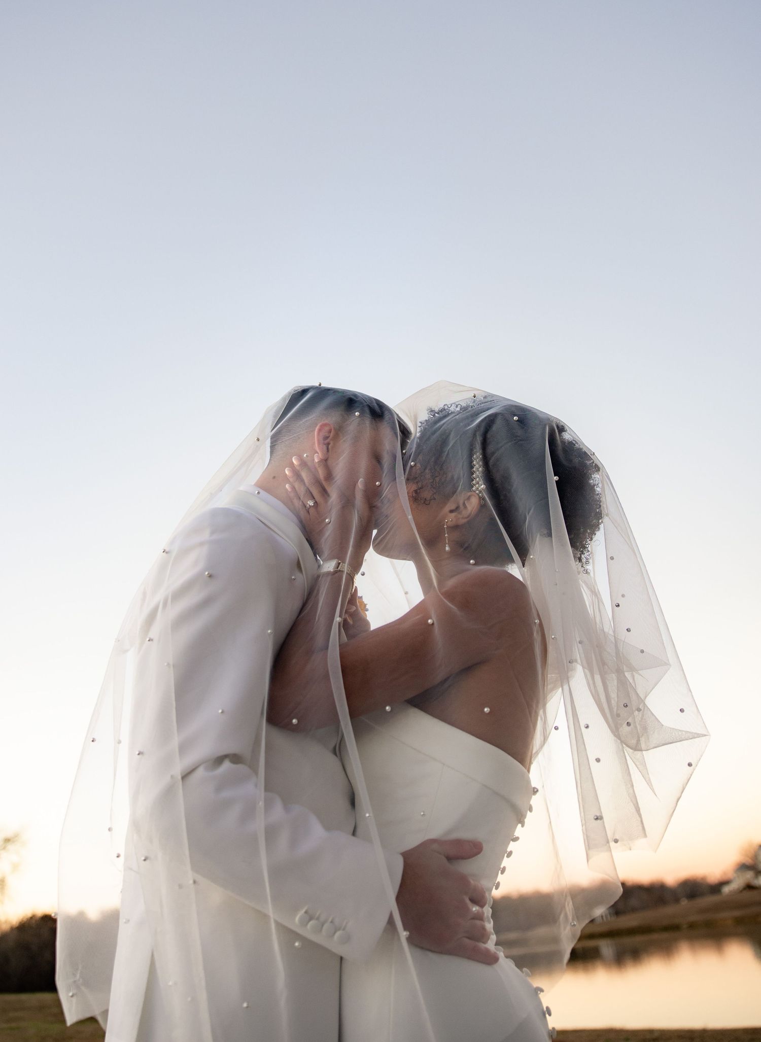 Romantic silhouette of newlyweds sharing intimate moments under a sunset sky by a serene lake.
