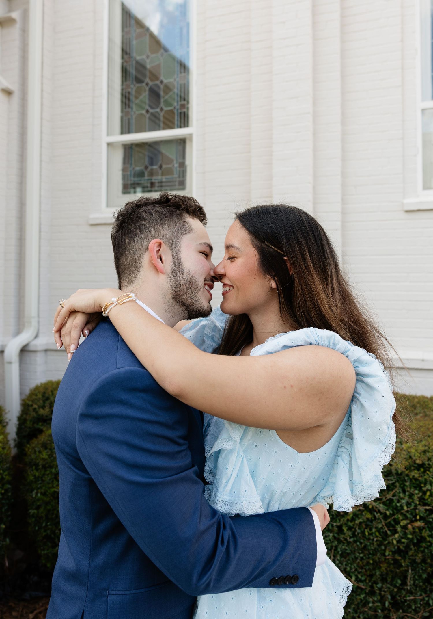 Couple sharing a romantic moment outside a church, man in navy suit embracing woman in light blue dress.